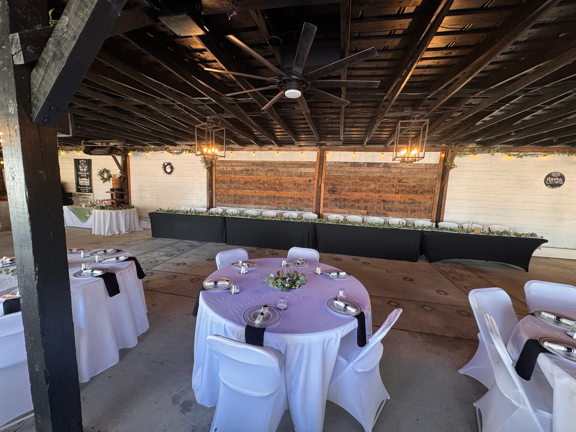Elegant wedding reception setup under a rustic wooden pavilion at Scarborough House featuring round tables with lavender overlays, white chair covers, black napkins, and a long head table adorned with greenery garland and warm string lights.