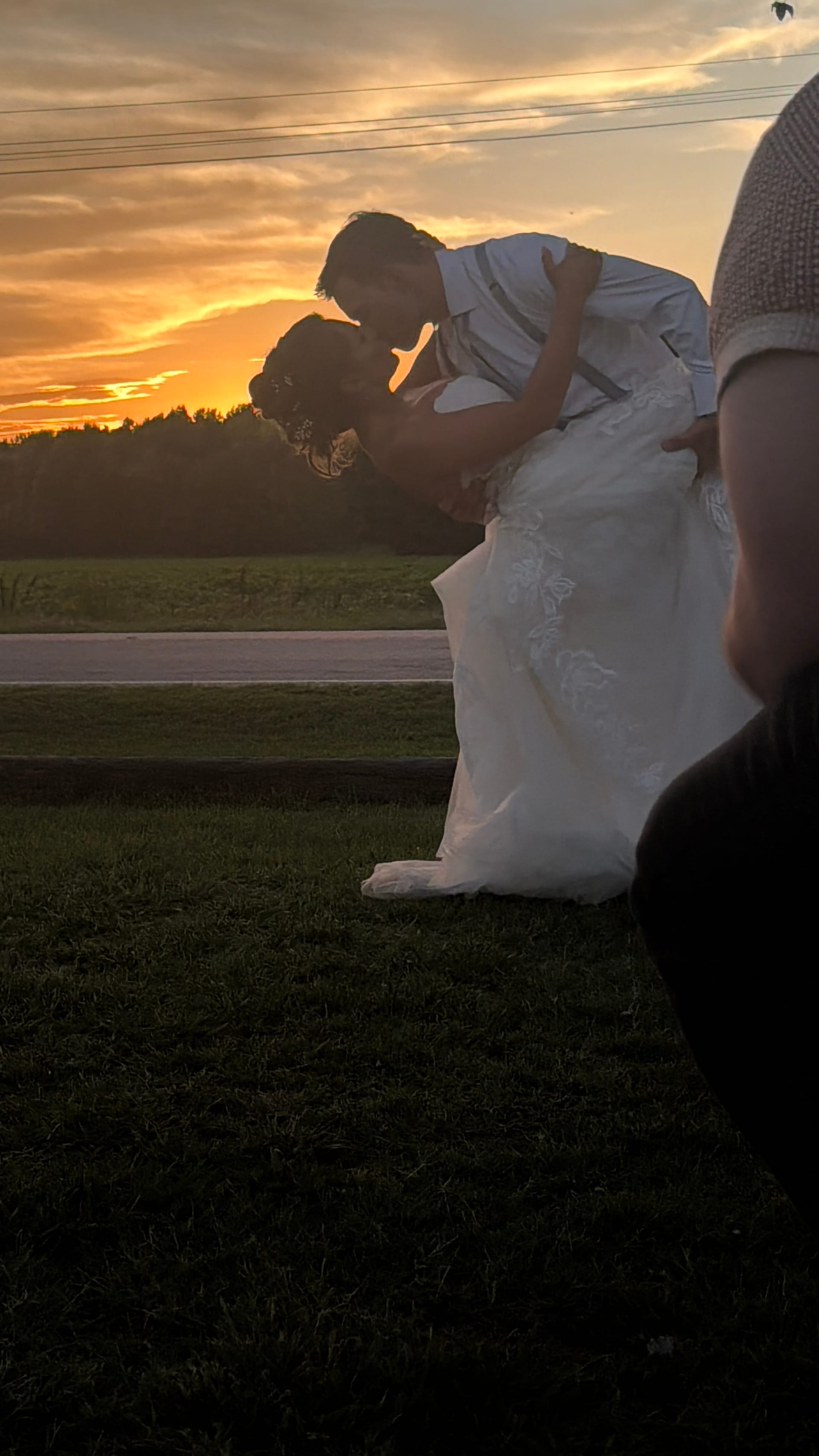 Groom dipping and kissing his bride in a lace wedding gown against a glowing orange and gold sunset sky on the ceremony lawn at Scarborough House.