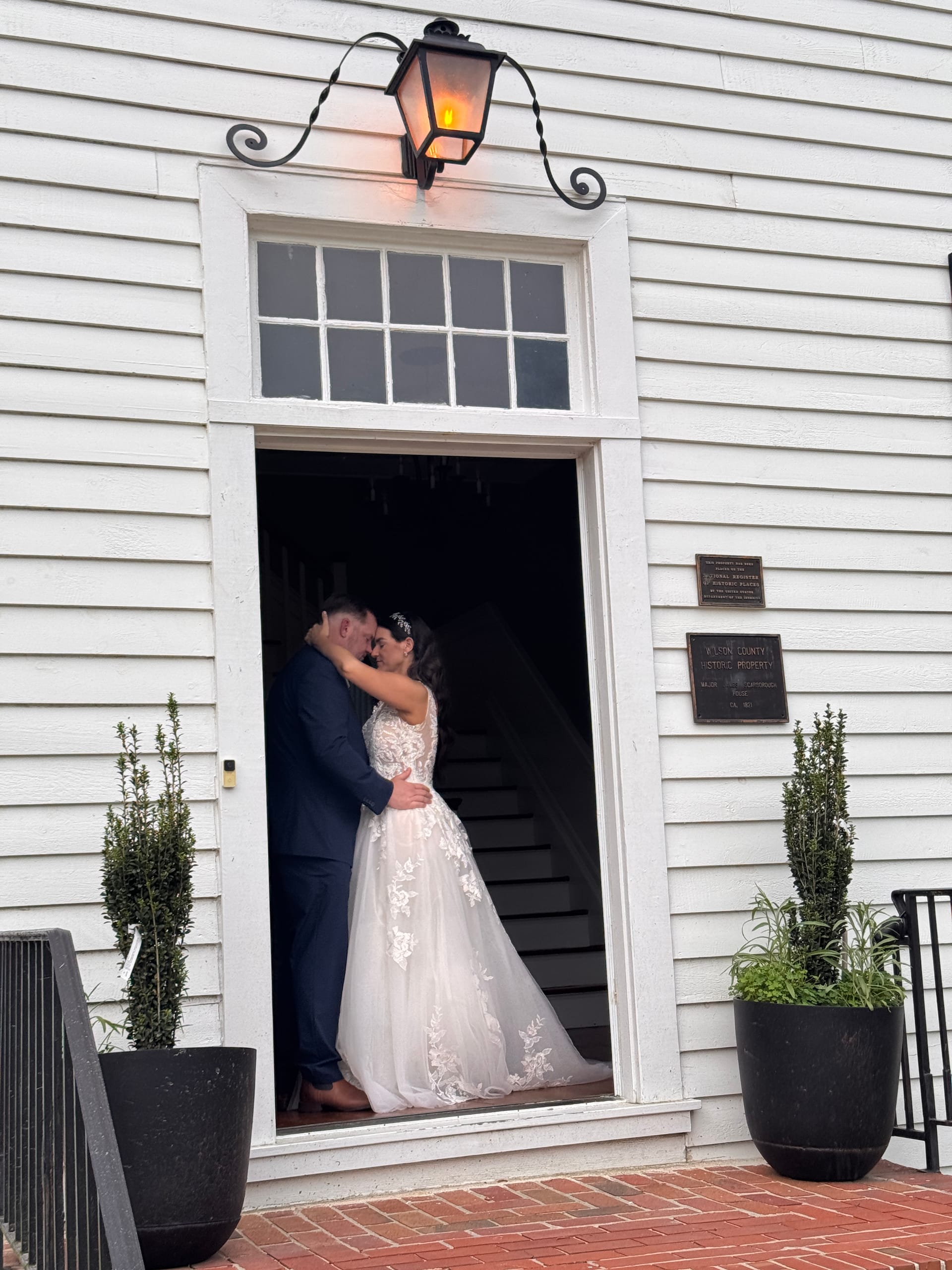 Bride in a lace ballgown and groom in a navy suit share an intimate forehead touch in the Scarborough House doorway.