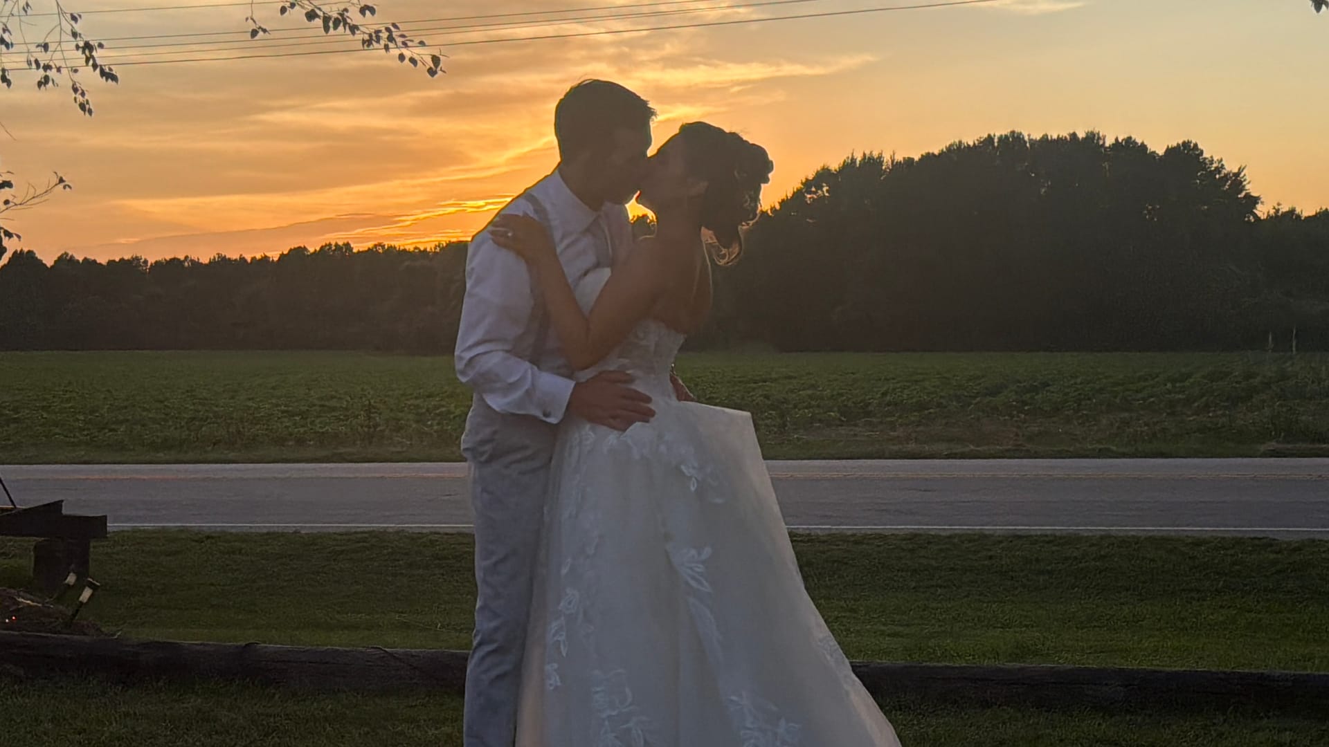 Bride and groom share a romantic kiss silhouetted against a glowing golden sunset over open farmland fields at Scarborough House estate.