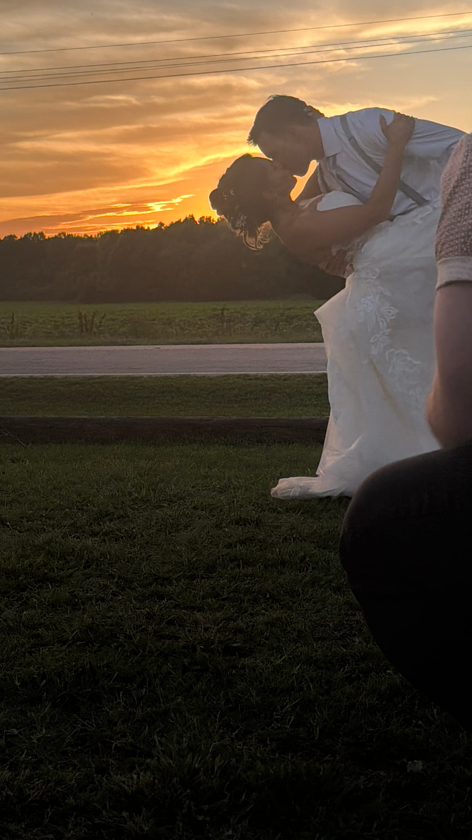 Bride and groom share a romantic dip kiss silhouetted against a glowing golden sunset sky over open farmland fields at Scarborough House.
