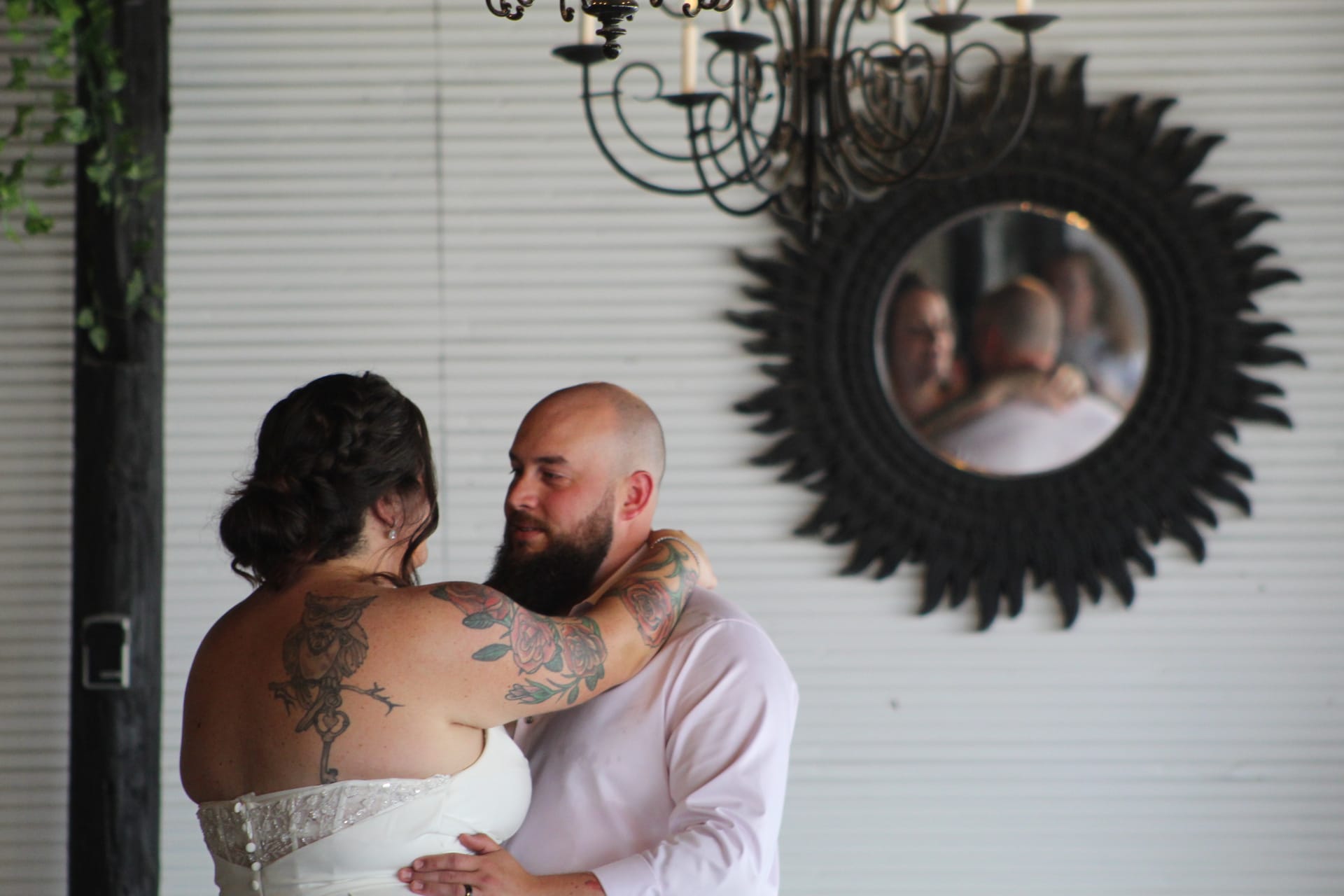 Bride and groom share an intimate first dance in the grand hall of Scarborough House, their reflection visible in an ornate sunburst mirror beneath a black wrought-iron chandelier.