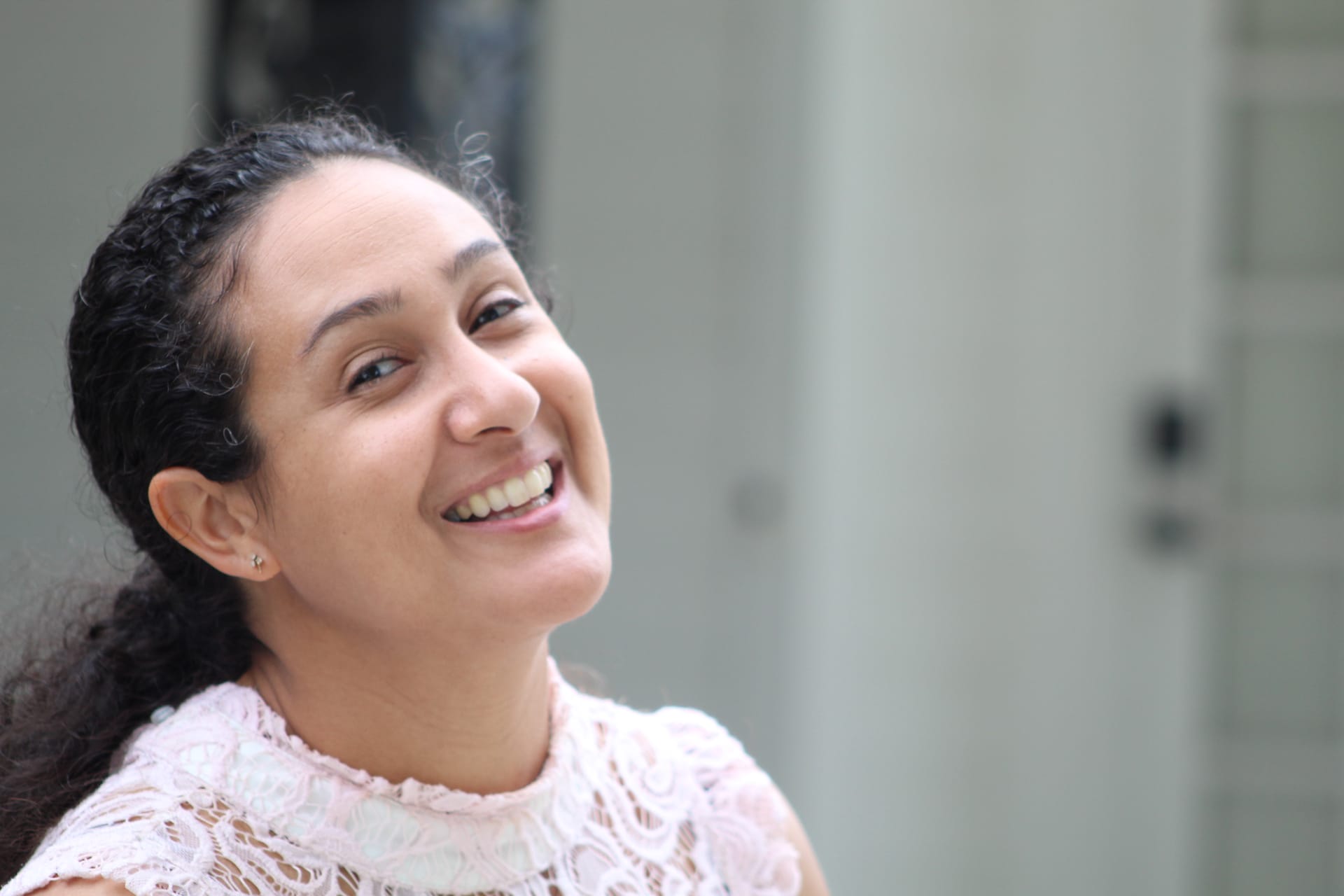 A smiling woman in a white lace top laughs joyfully outdoors against a softly blurred historic estate backdrop.