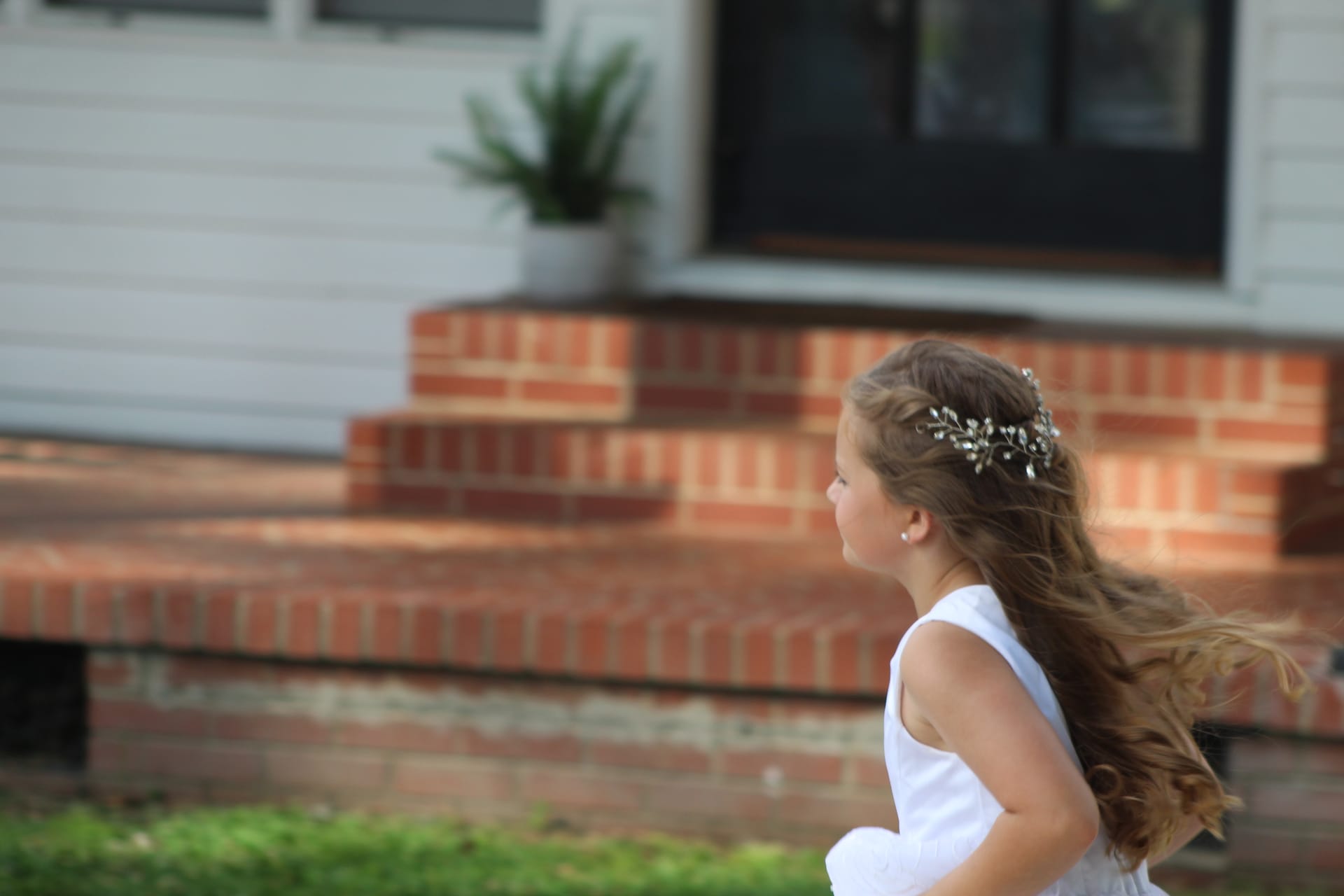 A flower girl in a white dress with long flowing hair and a crystal hair vine runs past the brick front steps of the historic Scarborough House manor.