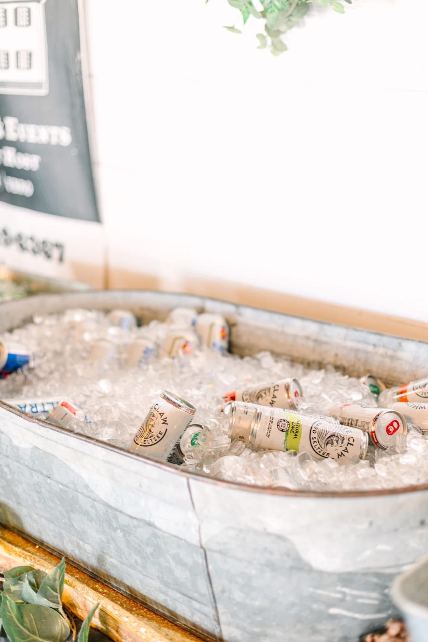 A galvanized metal tub overflowing with crushed ice and chilled White Claw hard seltzer cans displayed at a rustic wedding reception bar at Scarborough House.
