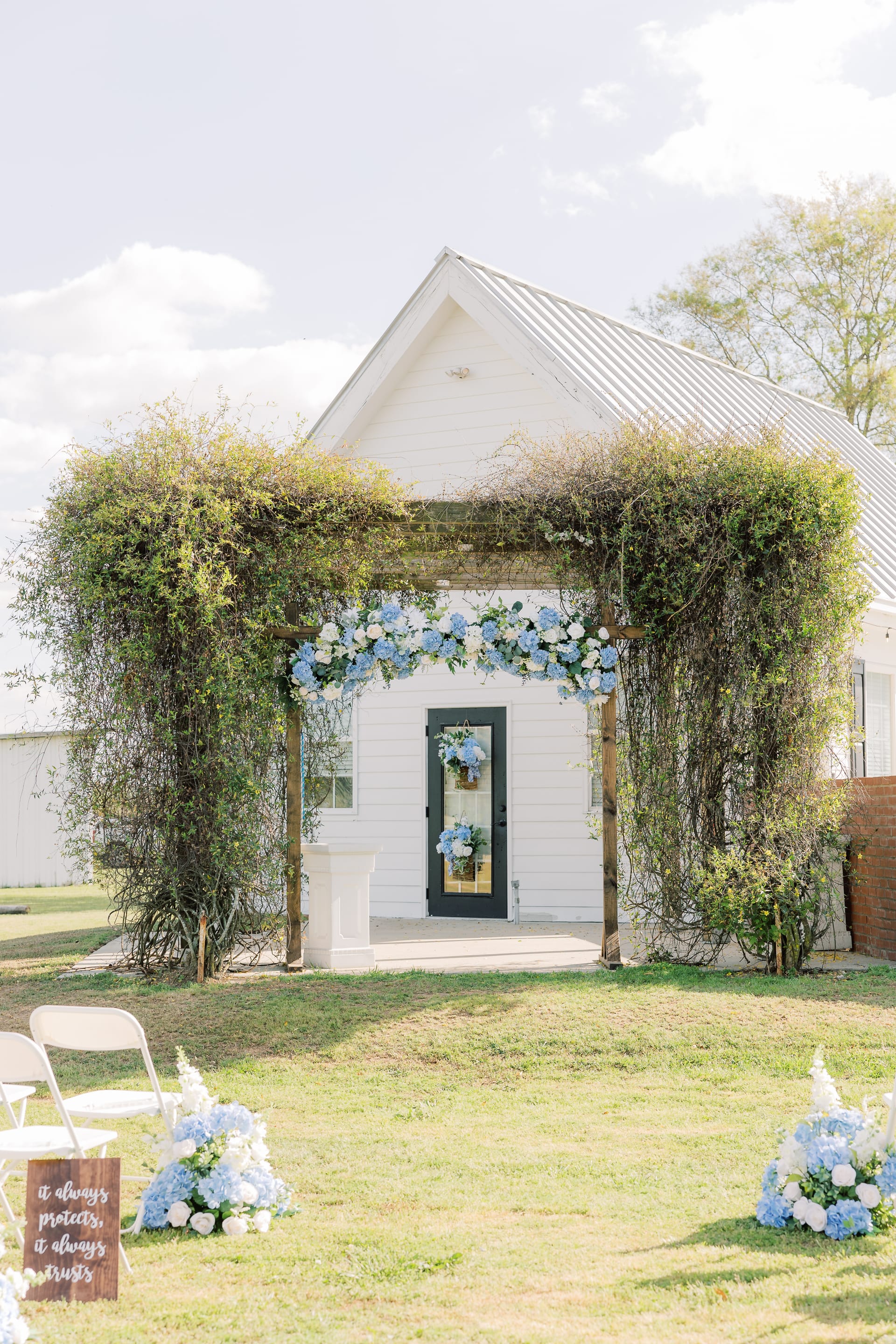 A vine-covered wooden arbor with blue and white hydrangea florals frames the chapel entrance at Scarborough House.