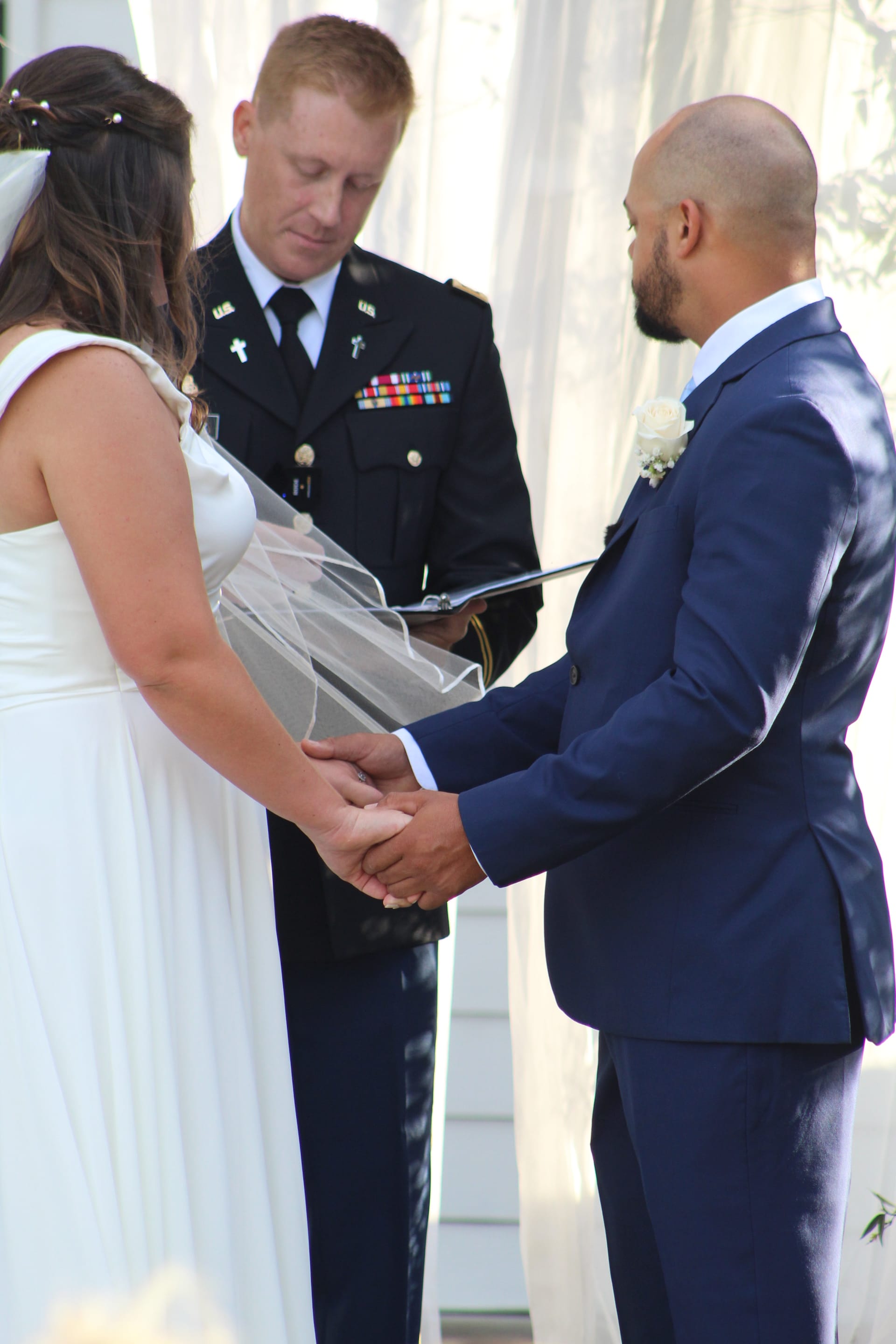 Bride and groom hold hands during outdoor wedding ceremony vows officiated by a military chaplain in dress uniform at Scarborough House historic estate.