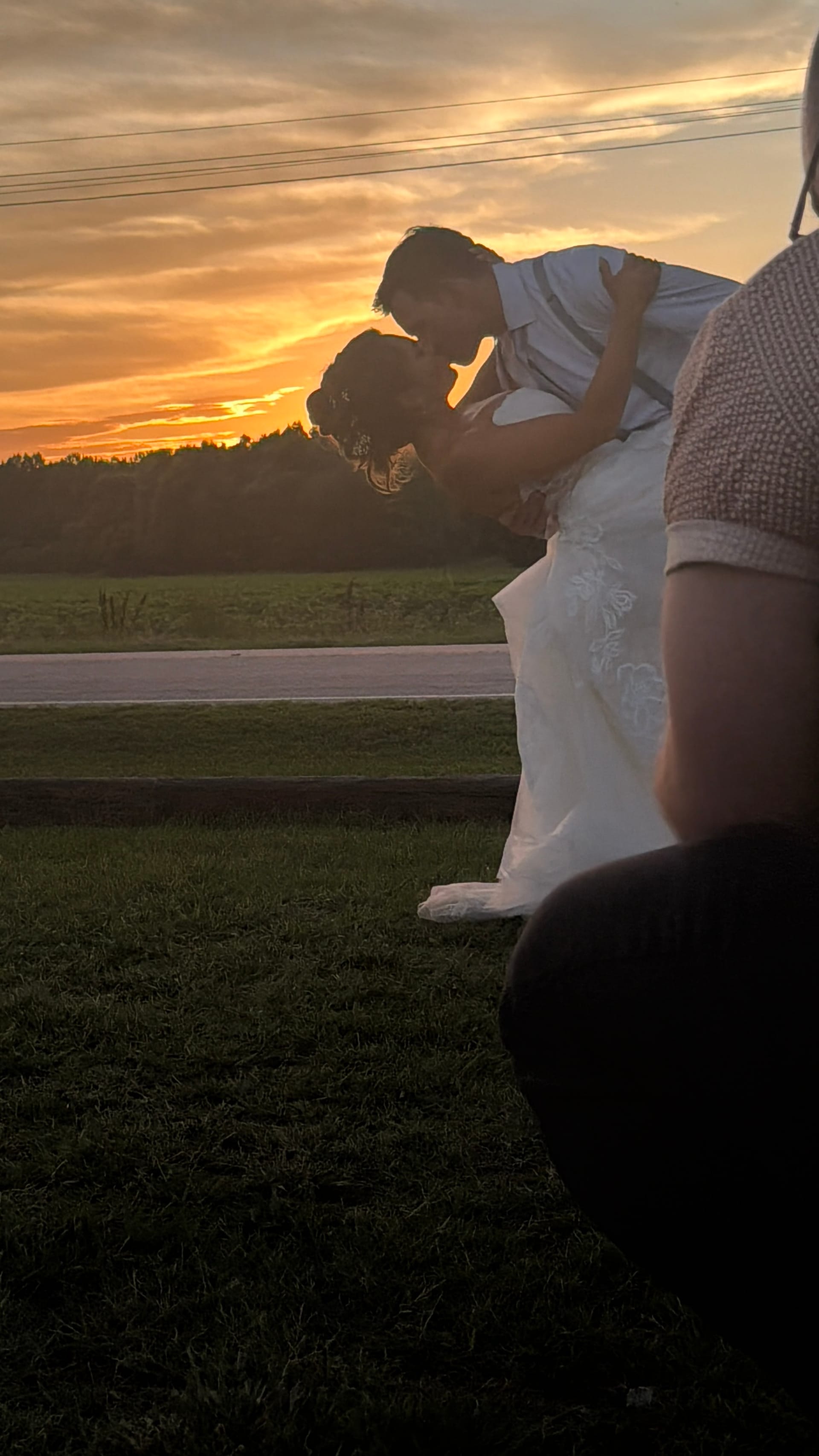 Groom dips and kisses bride in a silhouetted embrace against a glowing orange and gold sunset sky over open farmland fields at Scarborough House.
