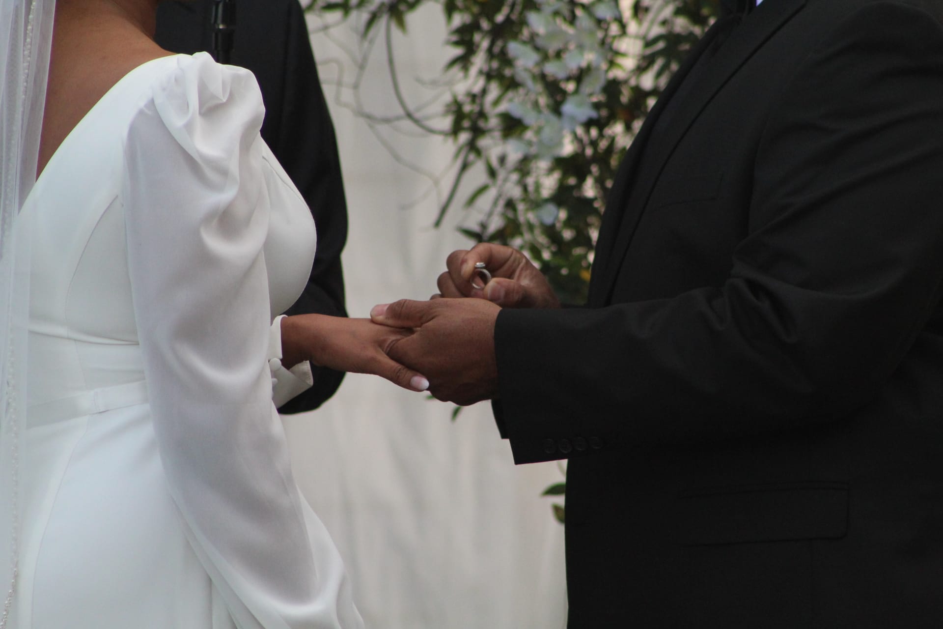 Groom placing a diamond wedding ring on the bride's finger during the ceremony at Scarborough House, with greenery and floral arch in the background.