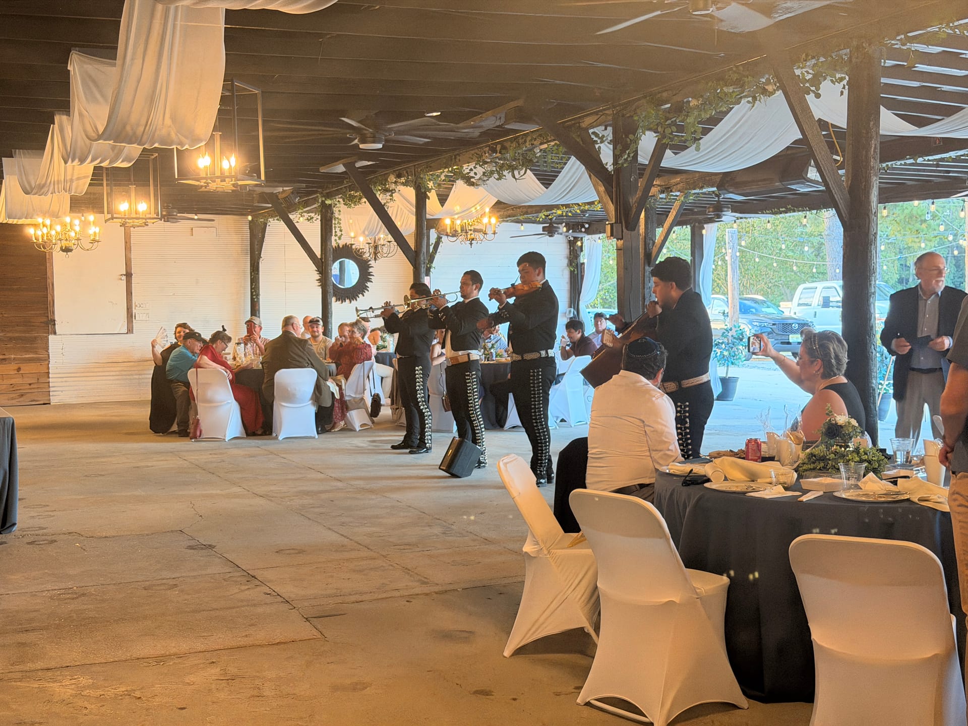 A mariachi band performs for seated wedding guests inside the rustic grand hall decorated with white draping and chandeliers at Scarborough House.