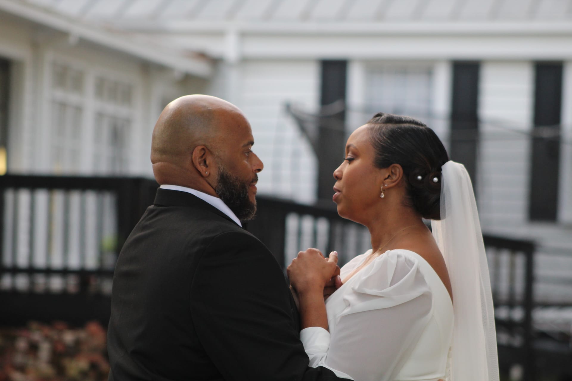 Bride in white off-shoulder gown and veil holds grooms hands as they share an intimate gaze during their outdoor wedding ceremony at Scarborough House historic estate.