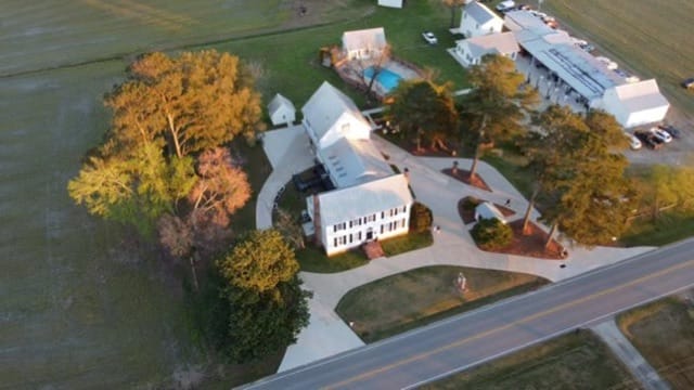Aerial drone view of Scarborough House historic estate at golden hour, showcasing the 1821 white manor house, sweeping circular driveway, mature oak trees, pool, and surrounding farmland fields.