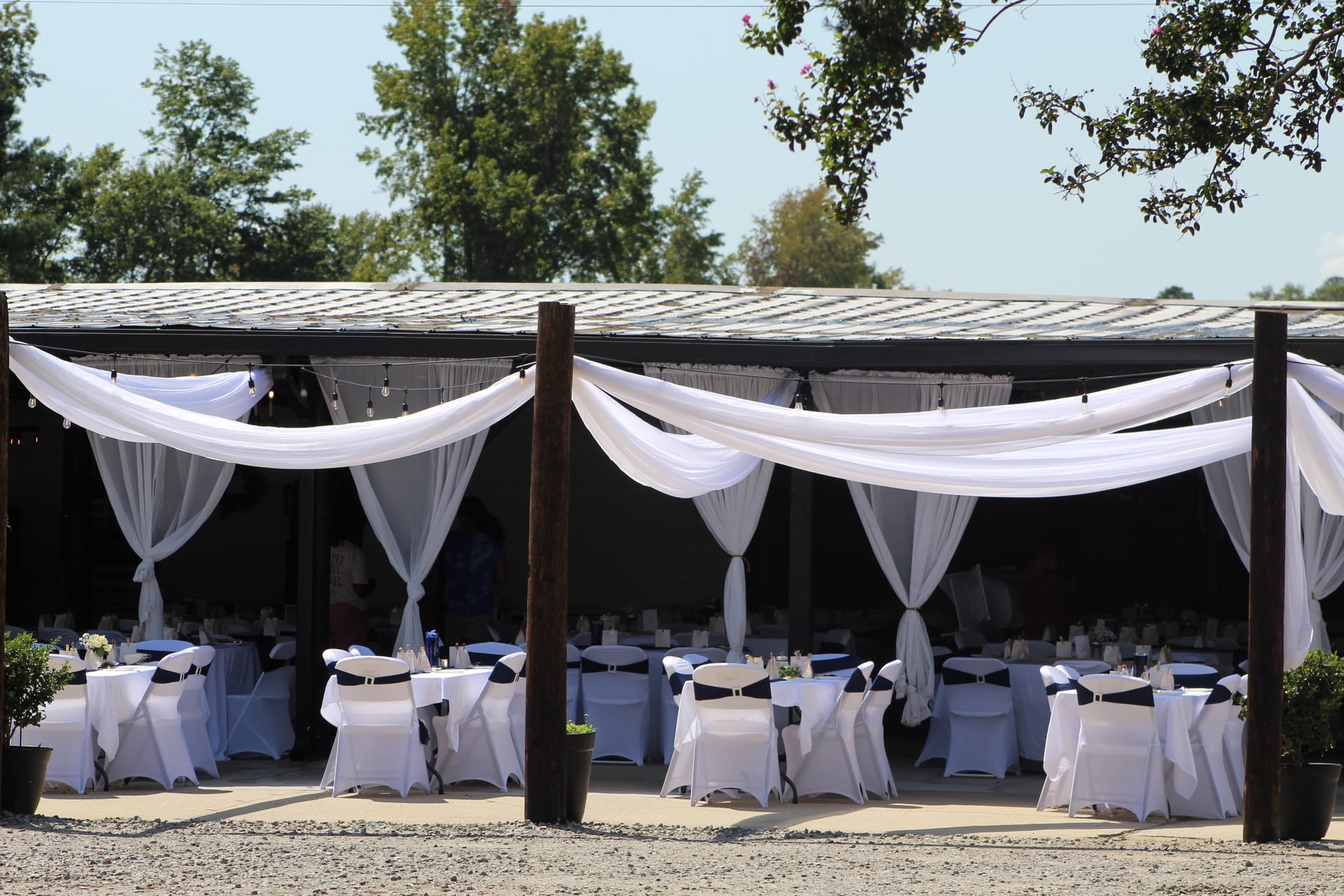 Elegantly decorated outdoor reception pavilion at Scarborough House featuring white draped fabric swags, round tables with white linens, and navy chair sashes set for a wedding celebration.