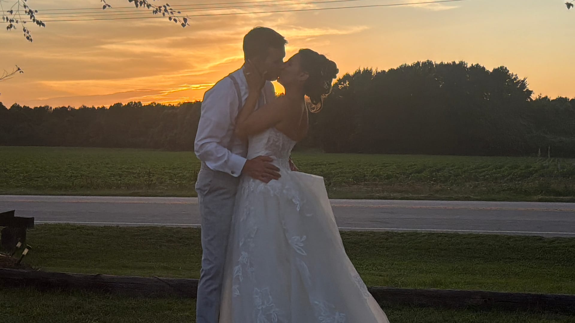 Bride and groom share a romantic kiss silhouetted against a vivid golden sunset over open farmland fields at Scarborough House wedding venue.