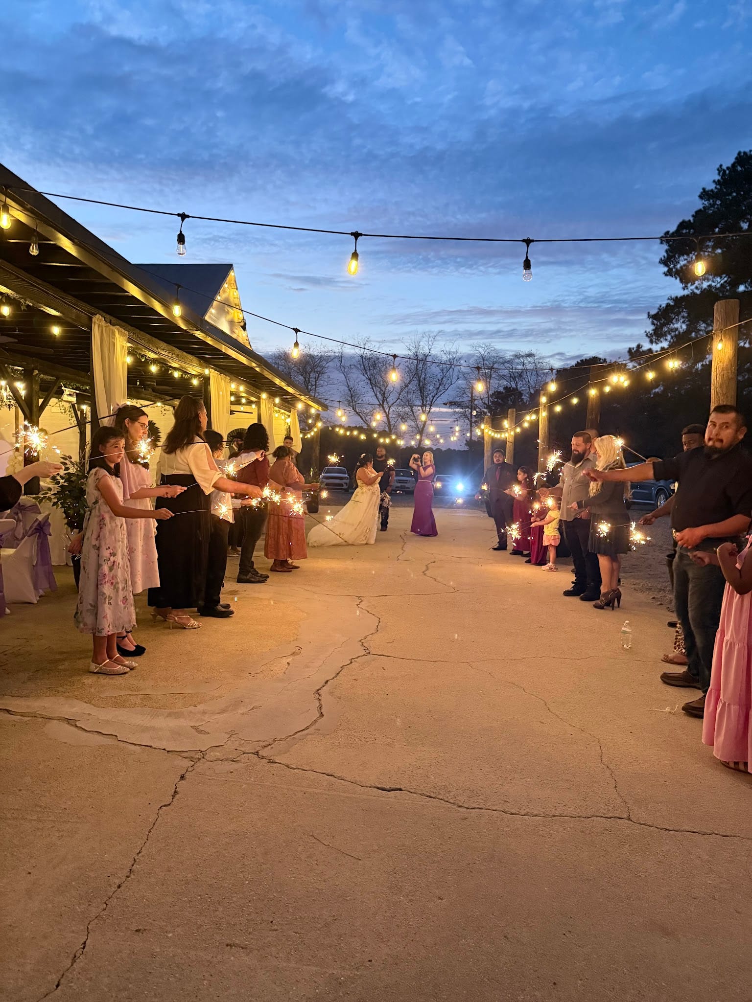 Wedding guests holding sparklers line a pathway under warm string lights at dusk as the newlyweds make their grand exit at Scarborough House.