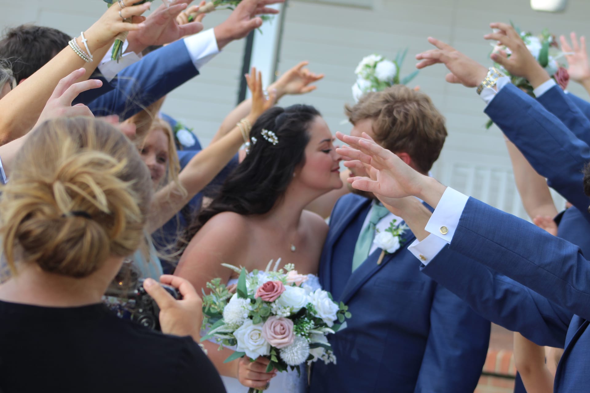 Bride and groom share a kiss beneath a raised-hands tunnel formed by their wedding party during their outdoor send-off at Scarborough House.
