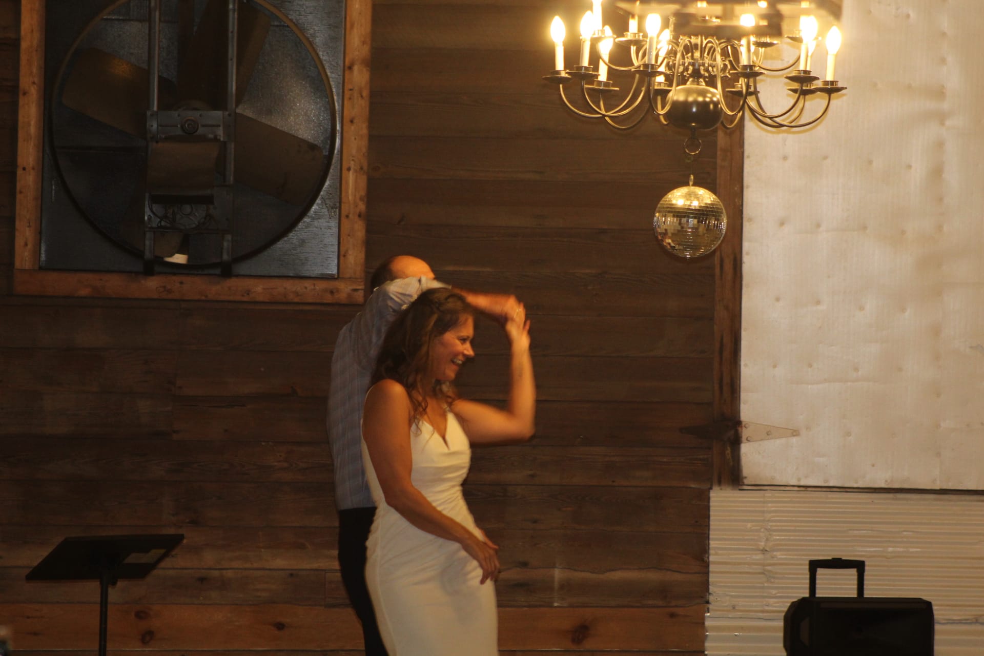 Bride in a white fitted gown laughs joyfully as her partner spins her during their first dance beneath a chandelier and disco ball in the warmly lit grand hall at Scarborough House.
