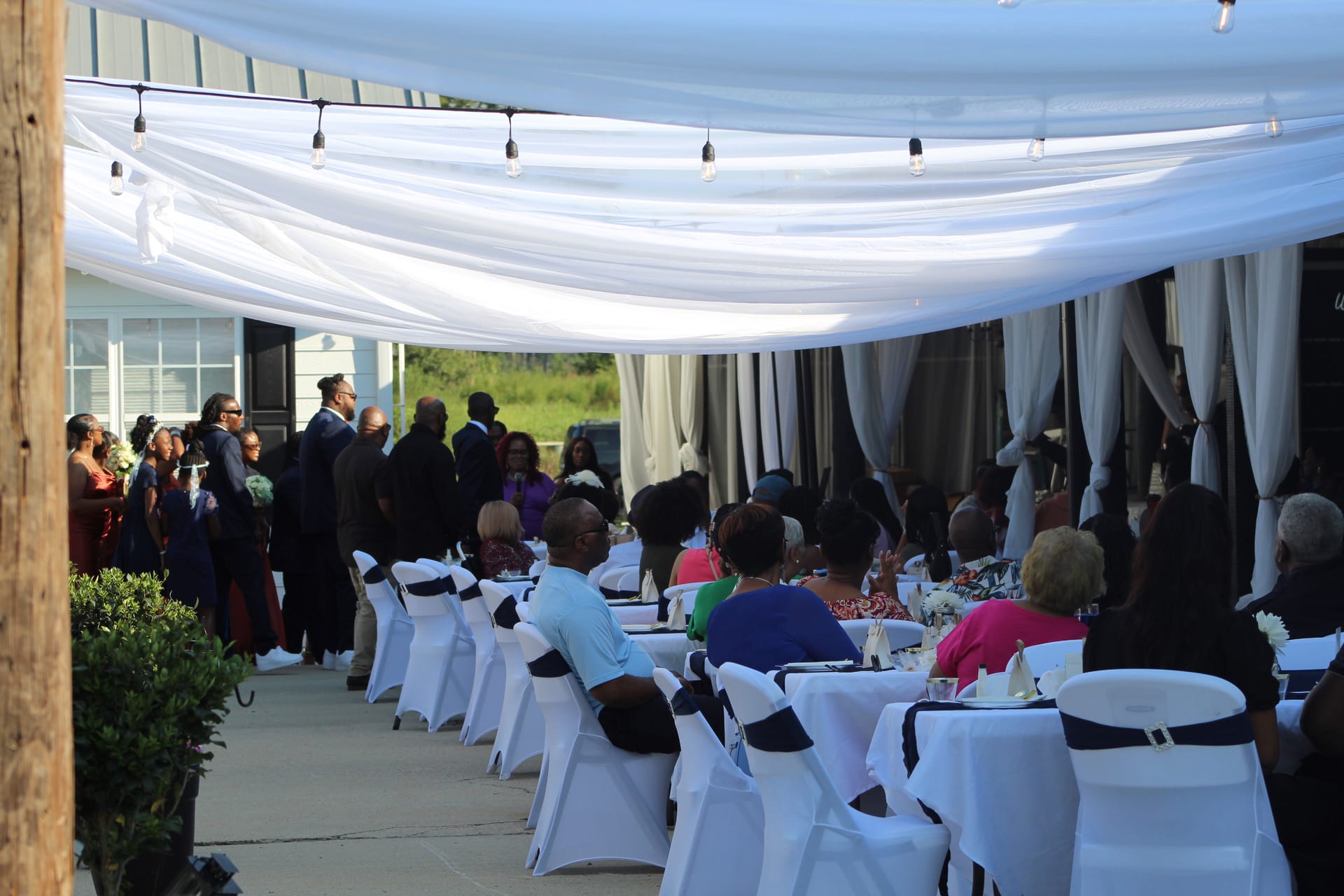Guests seated at elegantly decorated outdoor reception tables beneath a draped white fabric canopy with Edison bulb string lights at Scarborough House wedding venue.