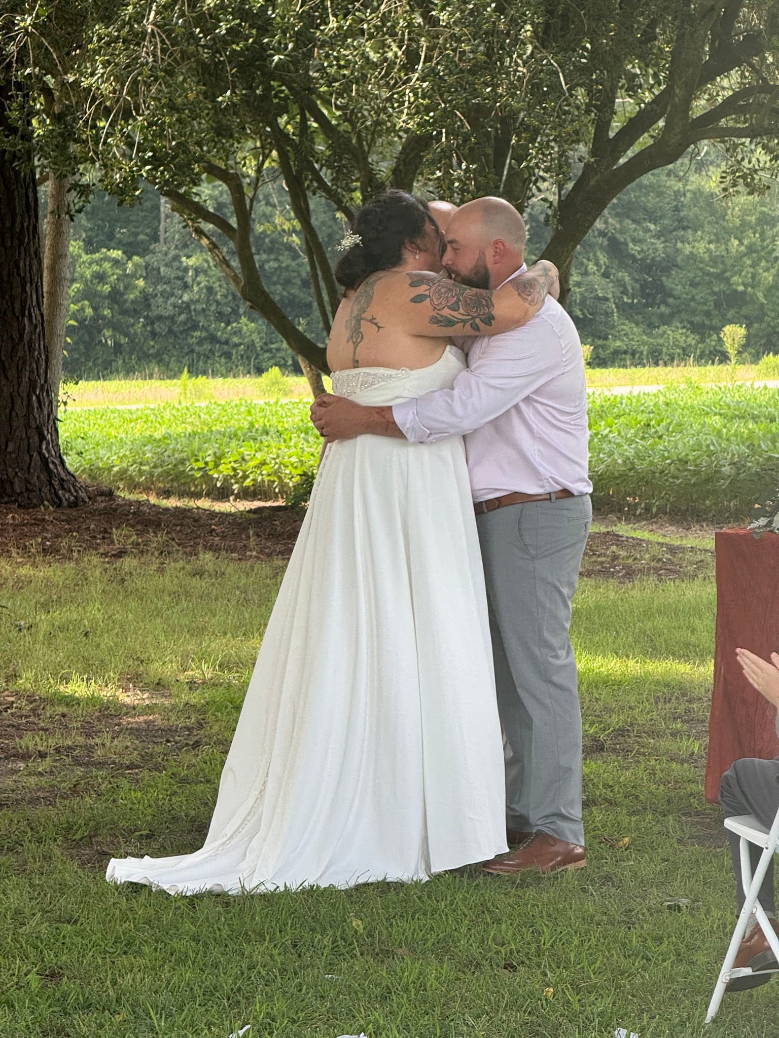 Bride and groom share their first kiss as a married couple on the ceremony lawn at Scarborough House, surrounded by towering oak trees and sunlit farmland fields.