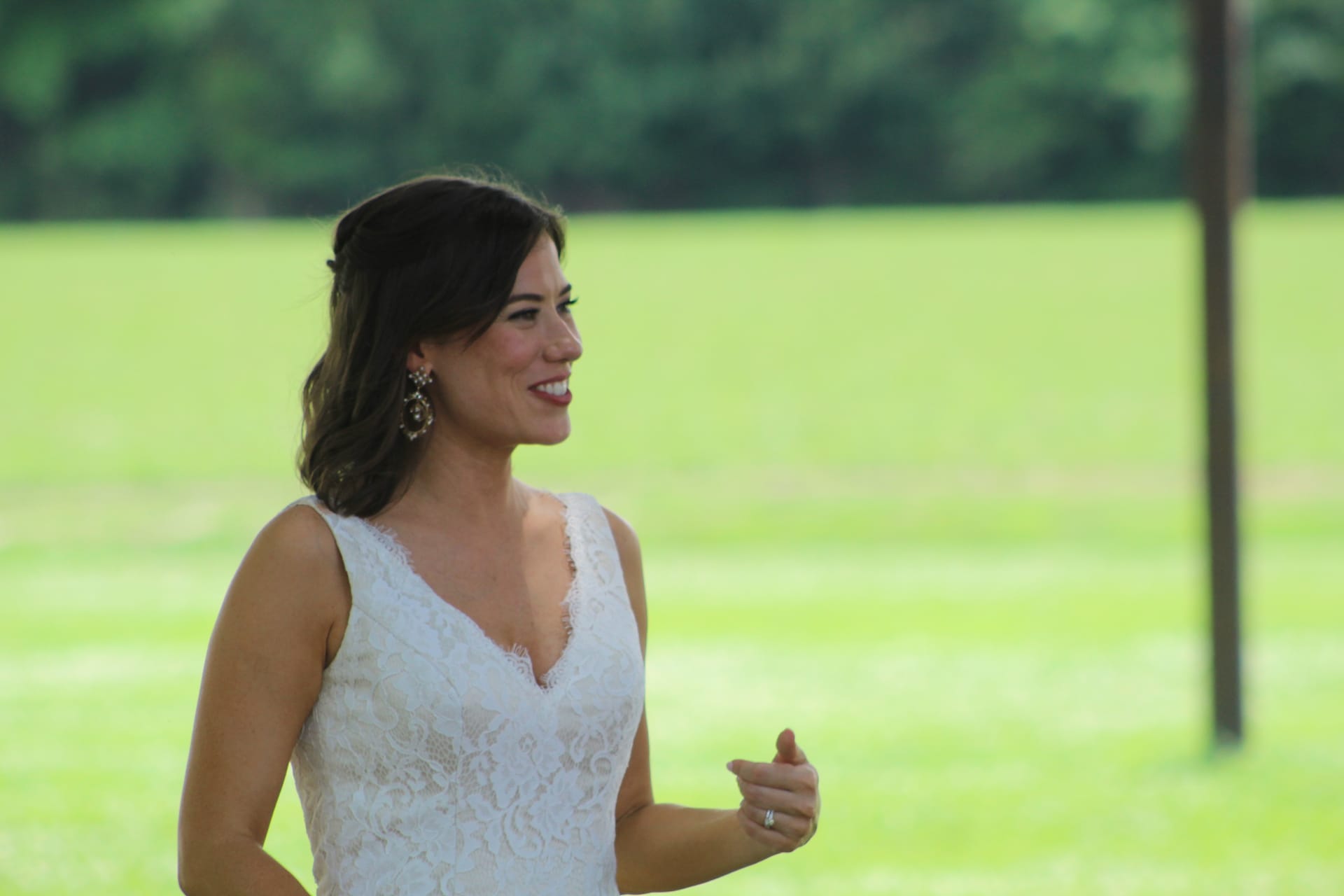 Smiling bride in a white lace gown standing on the ceremony lawn at Scarborough House with lush green fields and trees in the background.