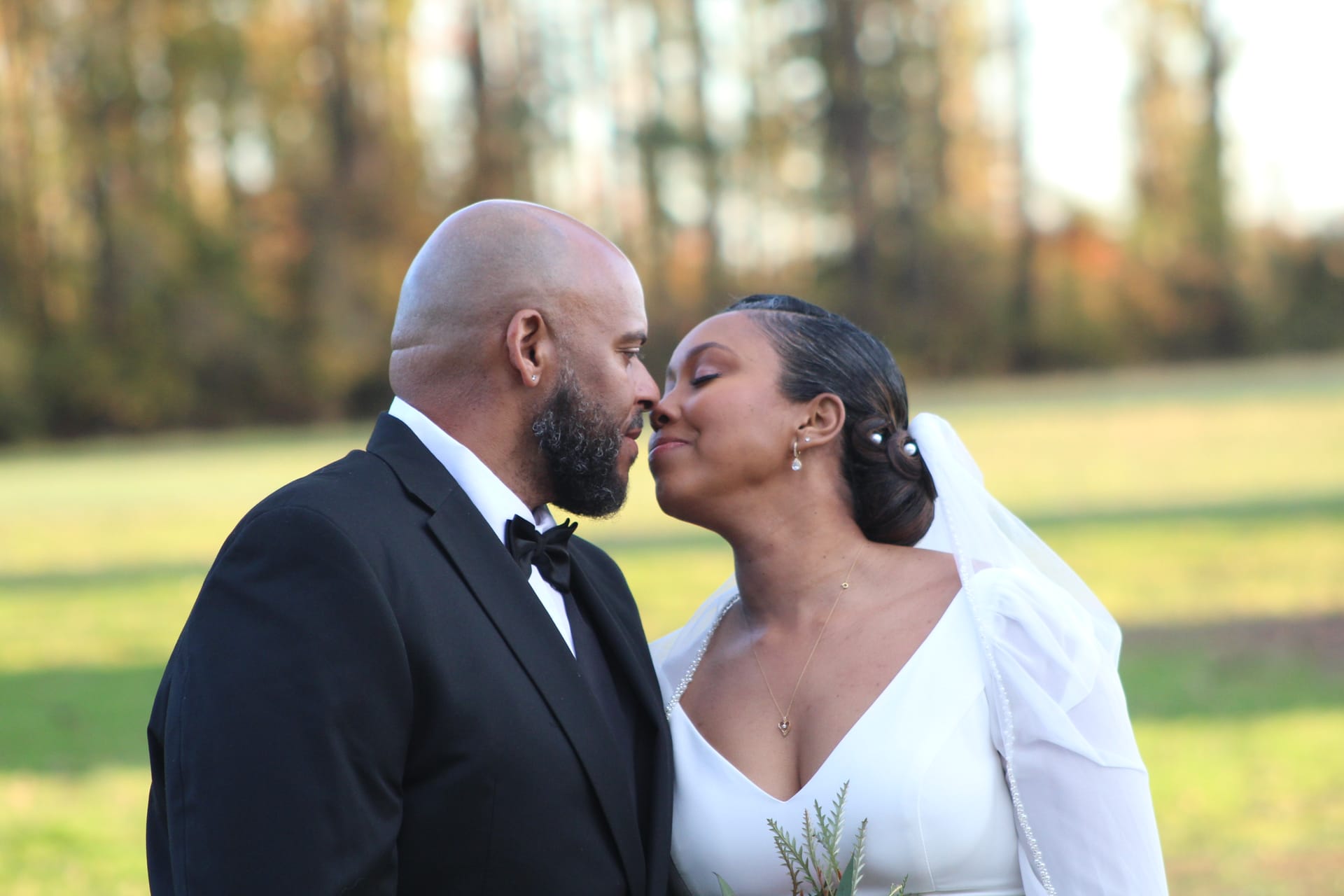 Bride in a white gown and veil leans in for a kiss with her tuxedo-clad groom against a softly blurred autumn landscape at Scarborough House.