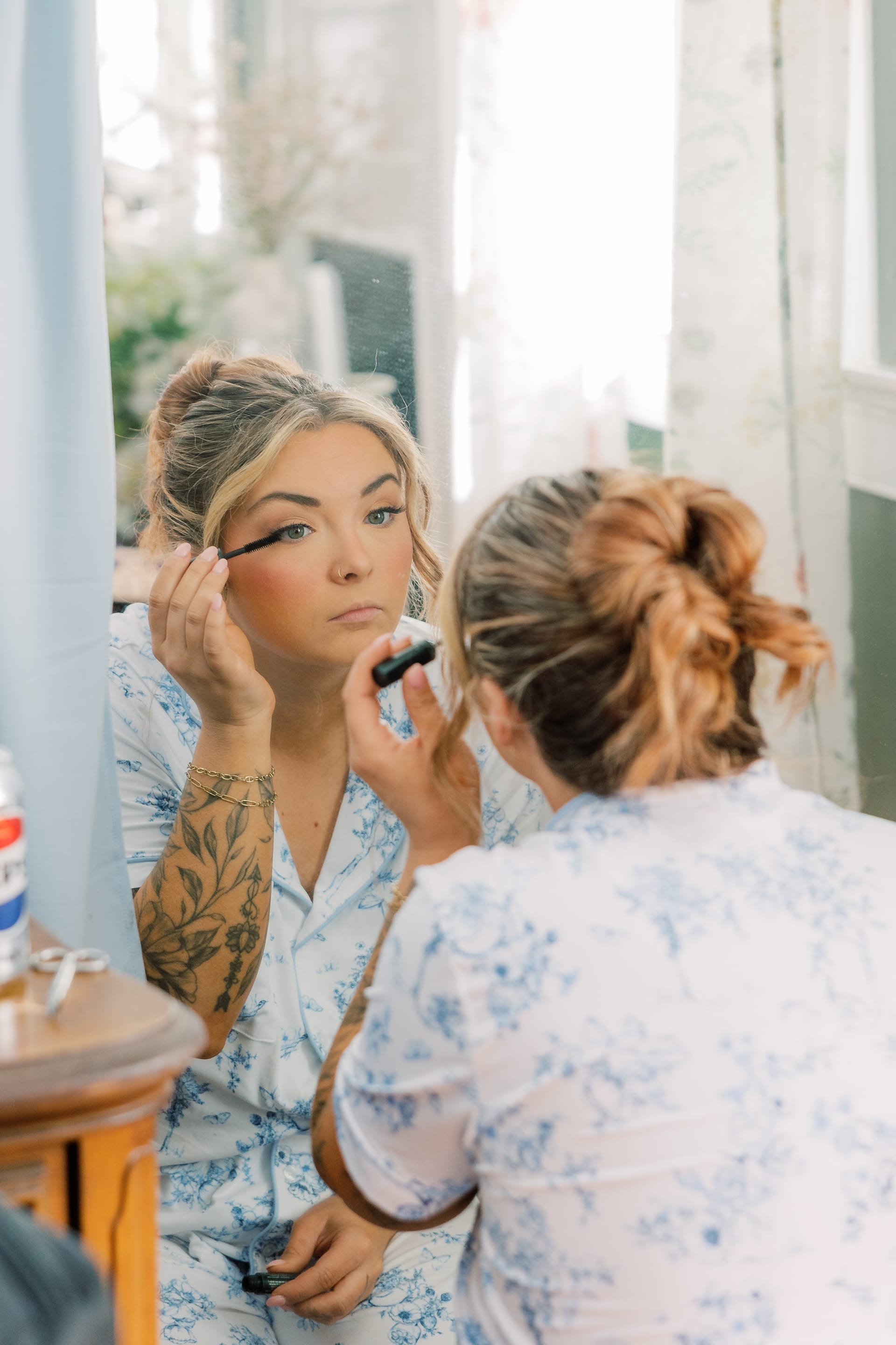 Bride in a blue floral robe applies mascara while looking into a mirror during wedding morning preparations at Scarborough House.