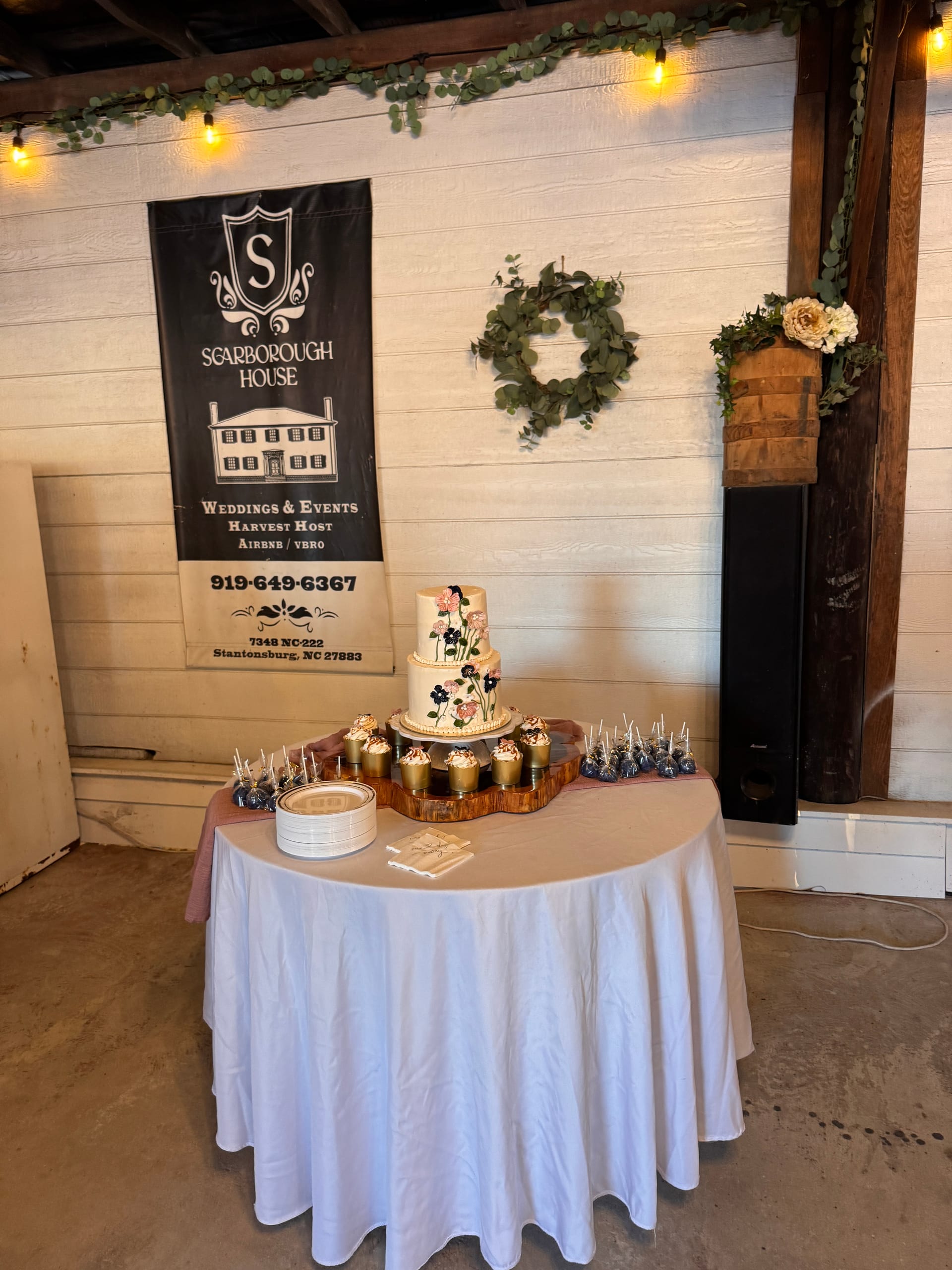 Elegant tiered floral wedding cake surrounded by gold cupcakes and cake pops on a draped table at Scarborough House wedding venue in Stantonsburg NC.