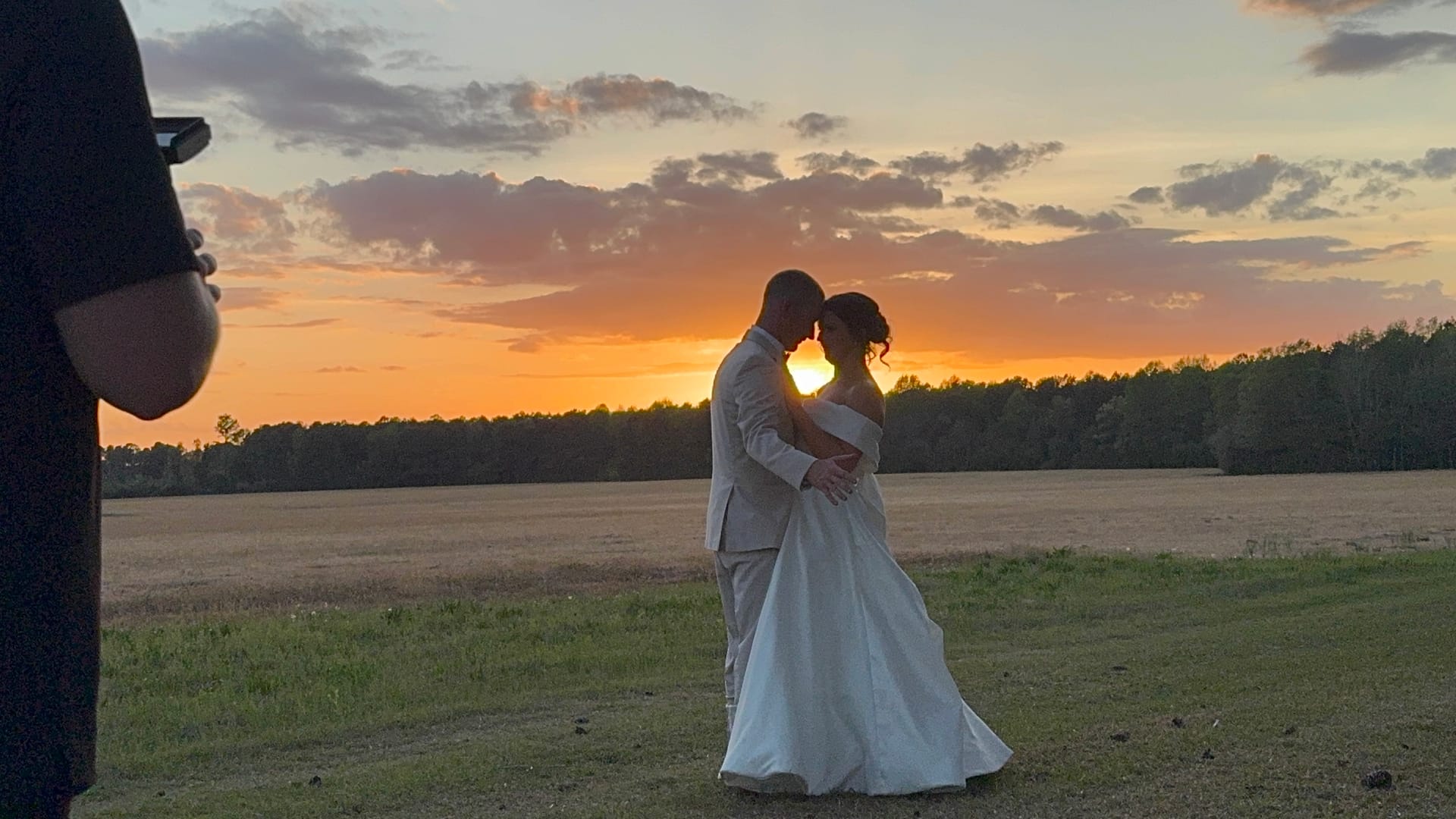 Bride and groom share an intimate forehead-to-forehead embrace silhouetted against a glowing orange sunset over the open farmland fields at Scarborough House.