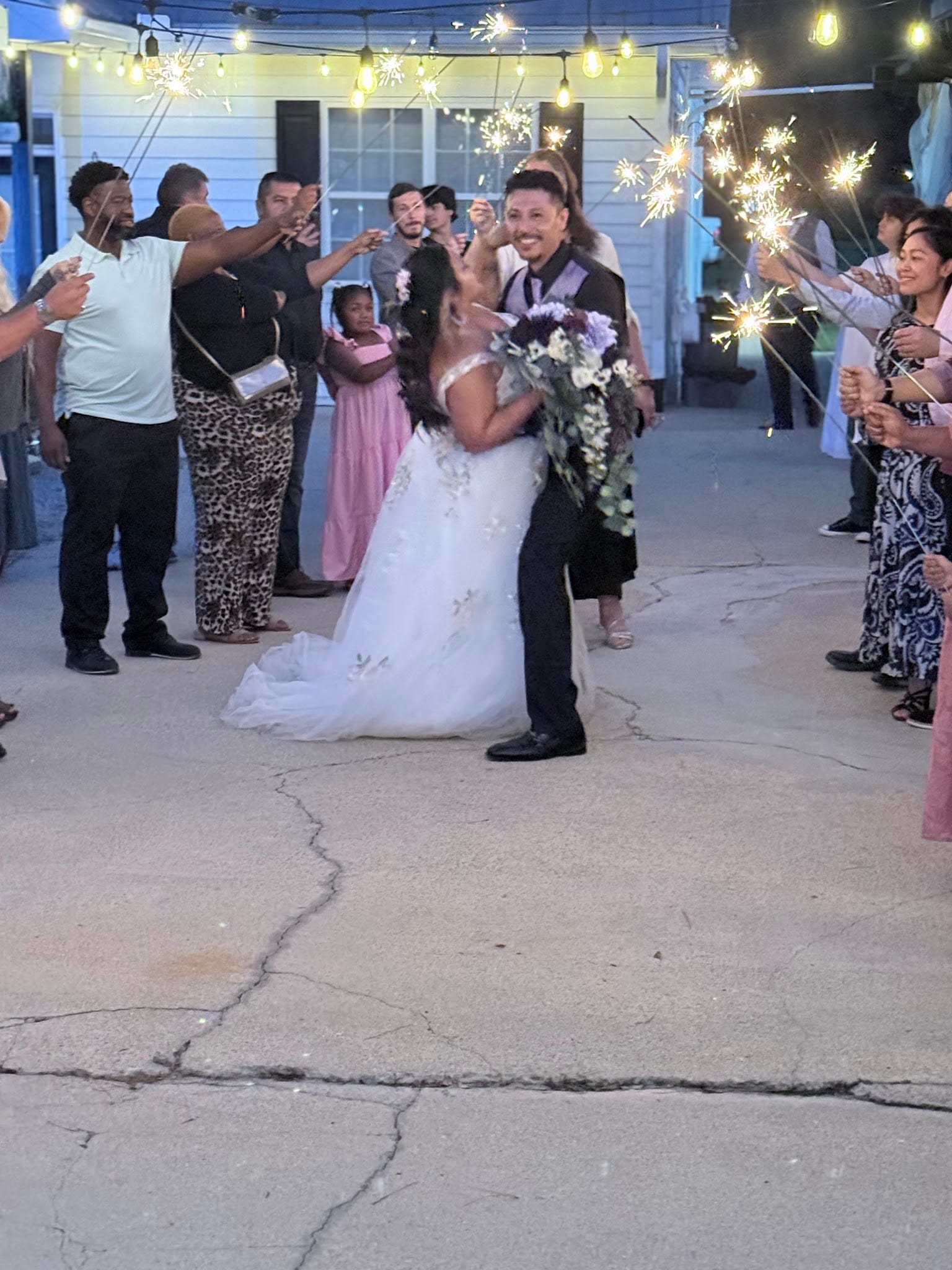 Bride and groom share a joyful embrace during a sparkler exit lined by cheering guests under warm string lights at Scarborough House wedding venue.
