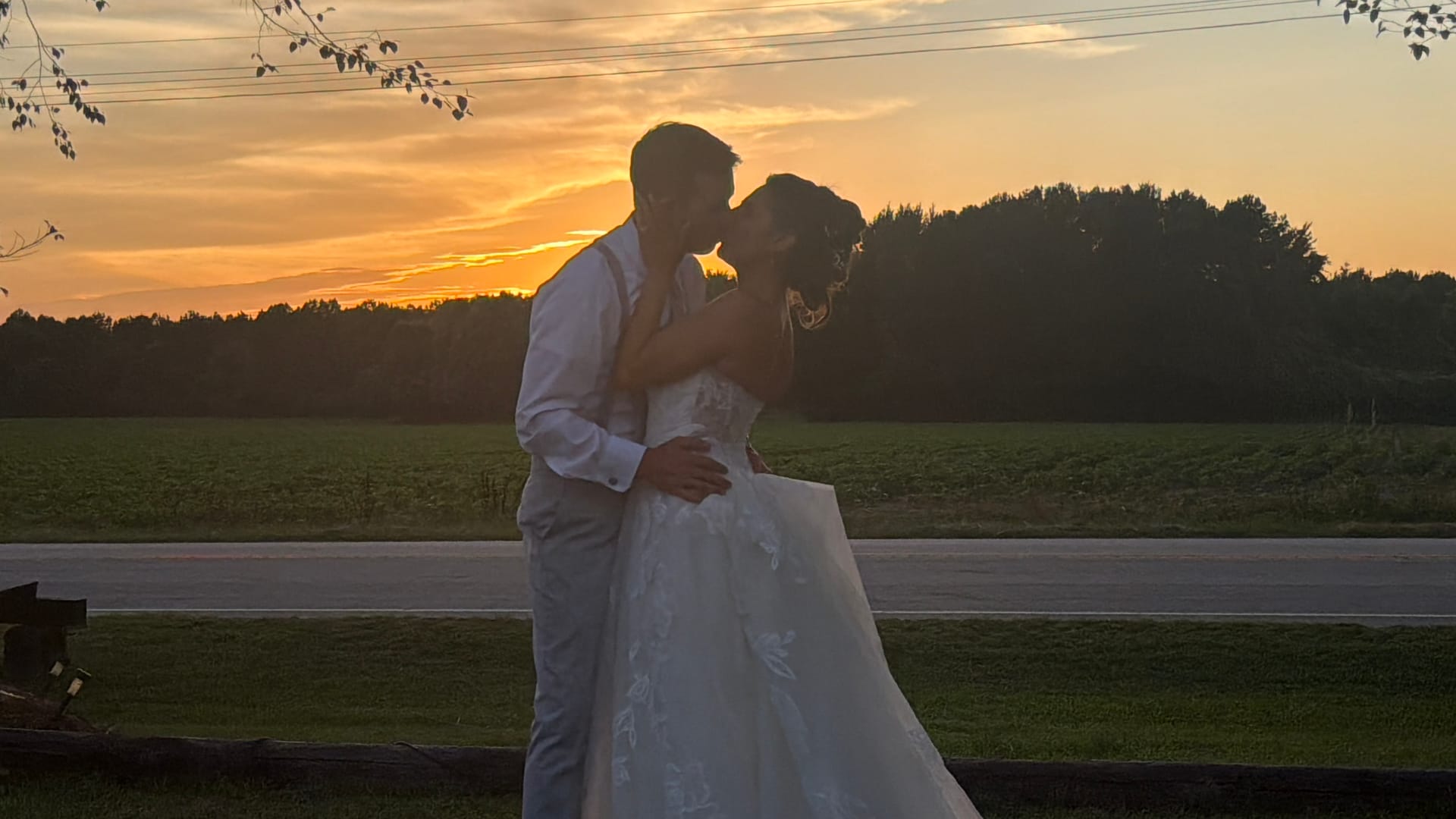 Bride and groom share a romantic kiss silhouetted against a vibrant golden sunset over open farmland fields at Scarborough House estate.