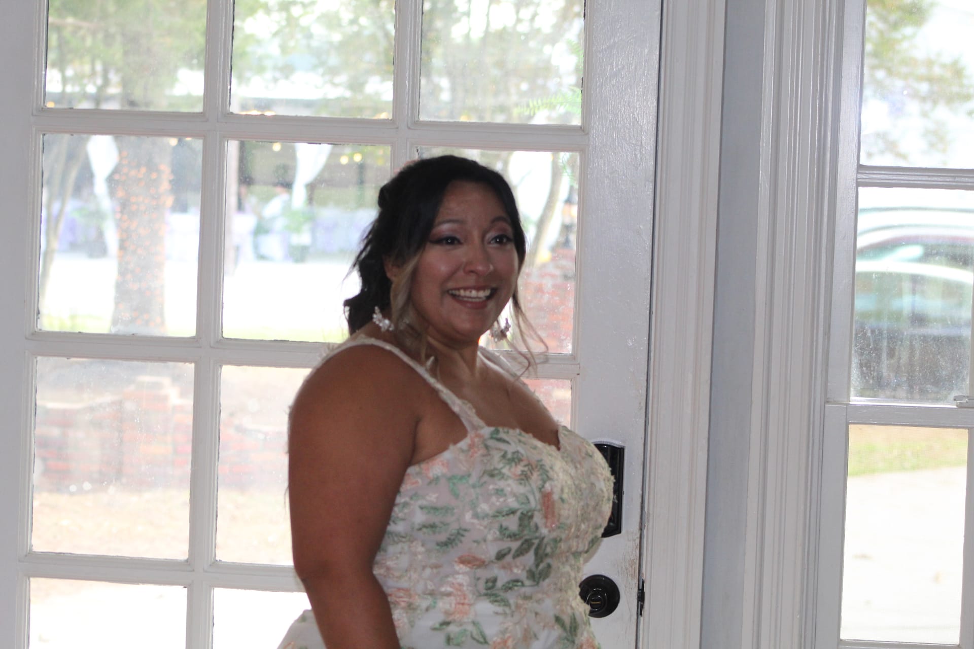 Smiling bride in a floral appliqué wedding gown standing at white French doors inside the Scarborough House historic venue.