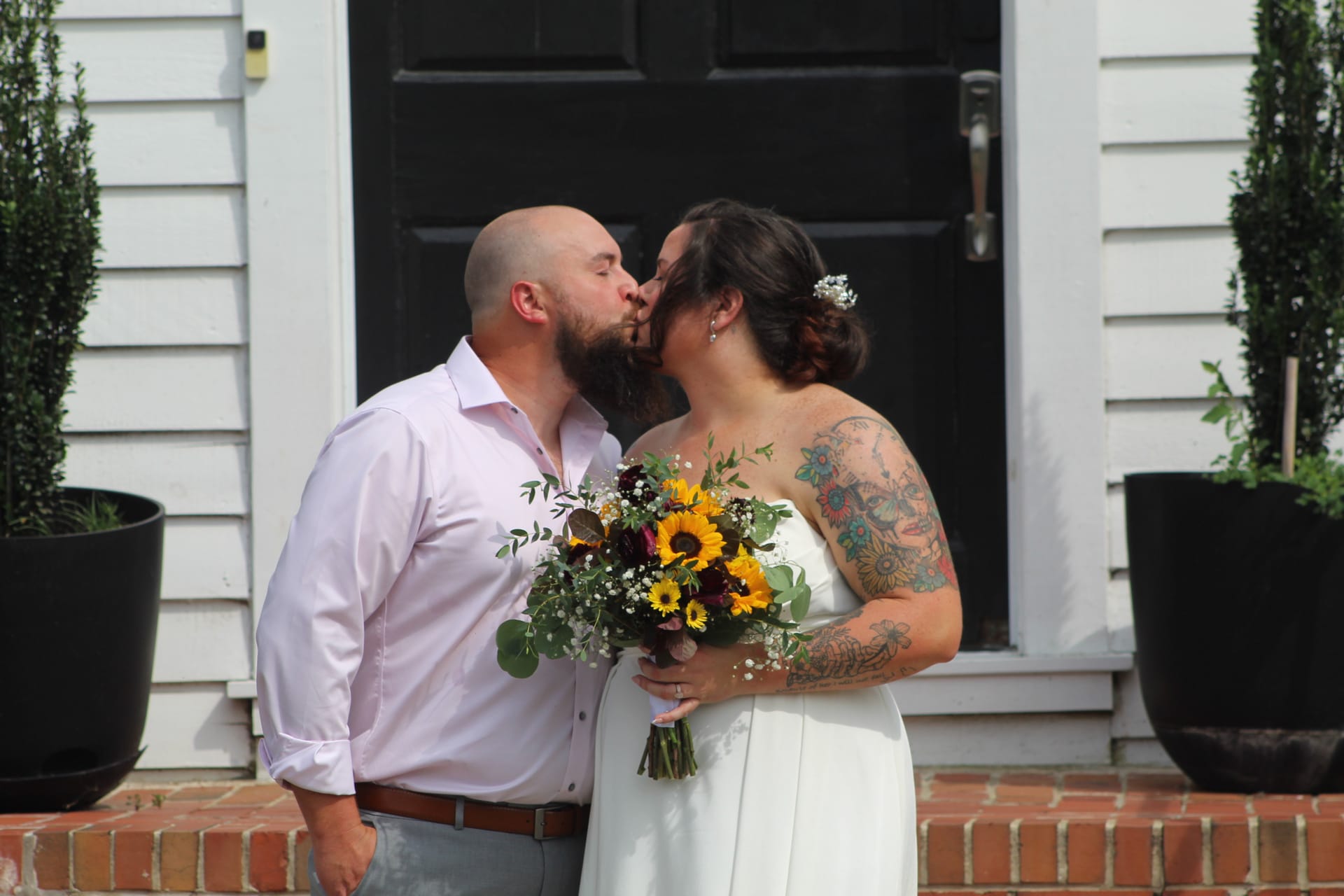 Bride and groom share a first kiss on the front steps of the historic 1821 Scarborough House estate, the bride holding a vibrant sunflower and greenery bouquet.