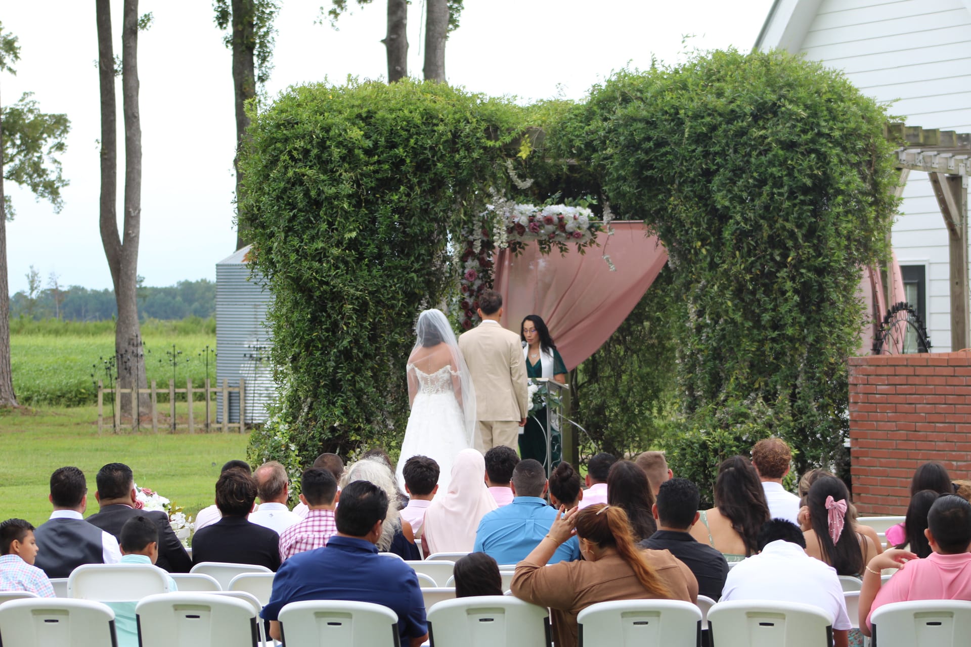 Bride and groom stand before a lush heart-shaped greenery arch adorned with pink draping and florals during an outdoor wedding ceremony at Scarborough House estate.