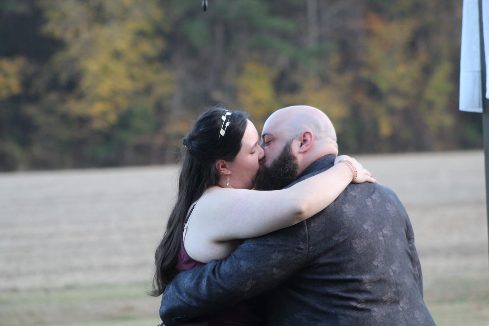 Bride and groom share their first kiss embrace on the ceremony lawn at Scarborough House with golden autumn trees in the background.