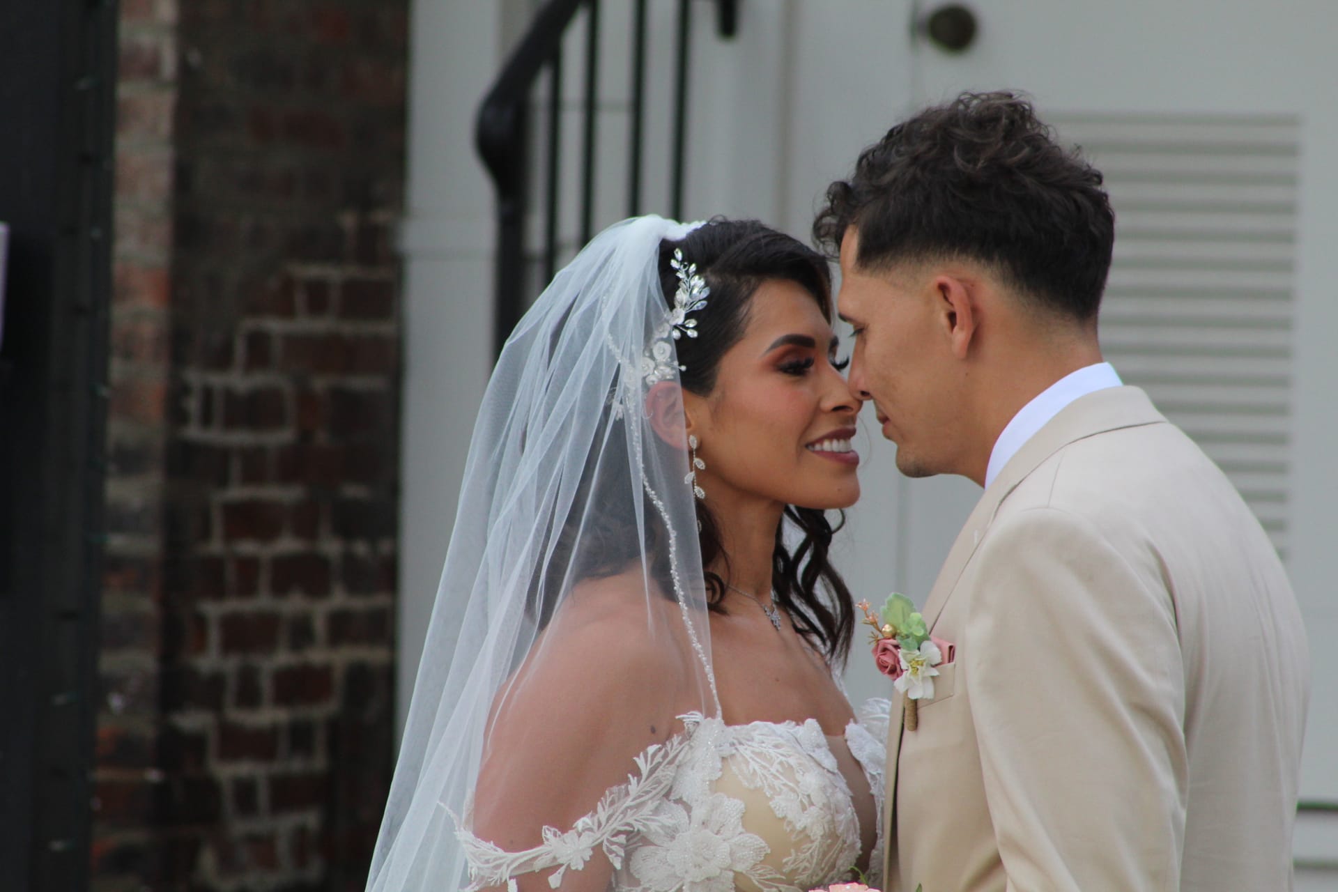 Bride in lace gown and veil smiling as groom in tan suit leans in close outside the historic Scarborough House manor.