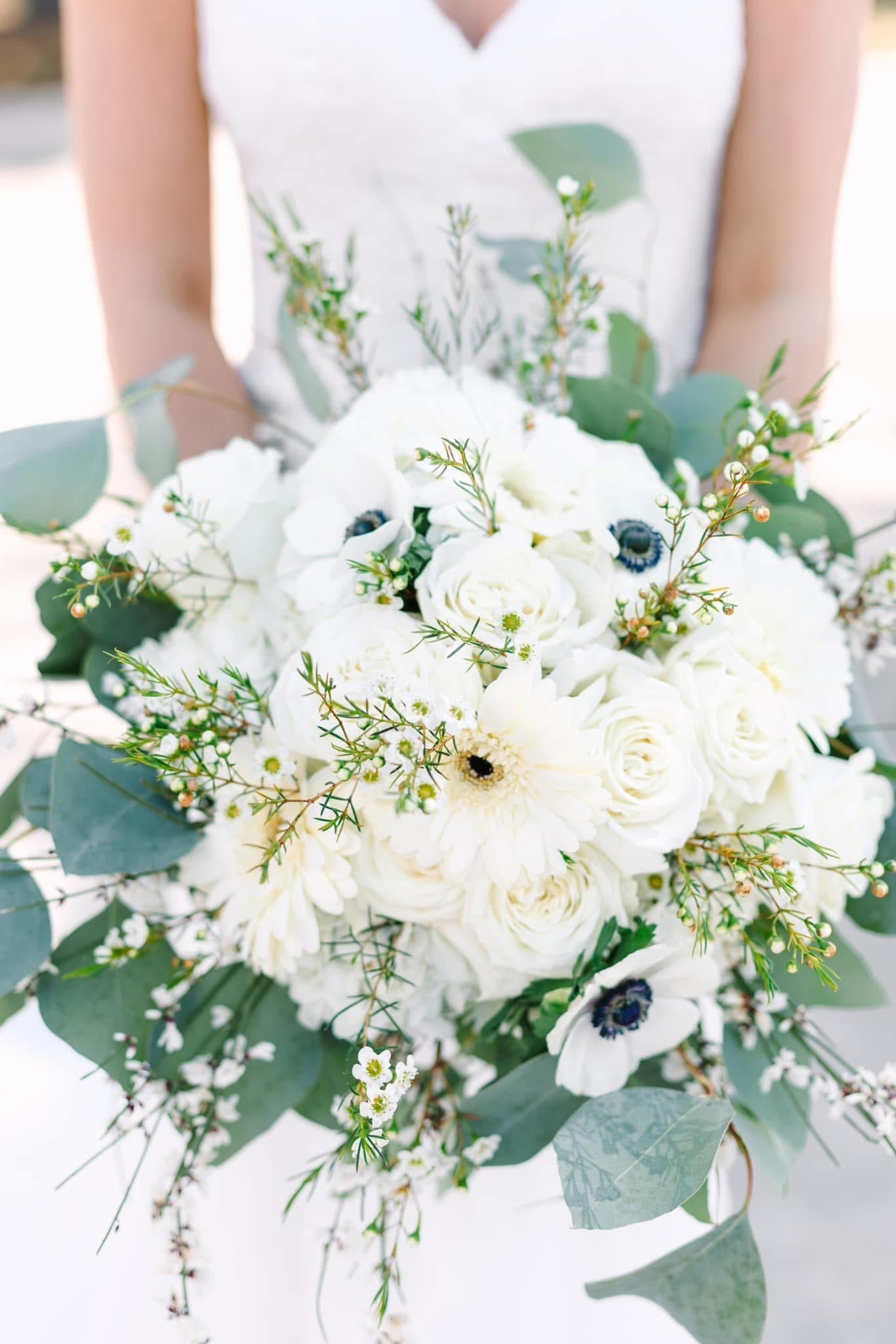 Bride holding a lush white bridal bouquet featuring roses, anemones, gerbera daisies, wax flowers, and eucalyptus greenery at Scarborough House wedding venue.
