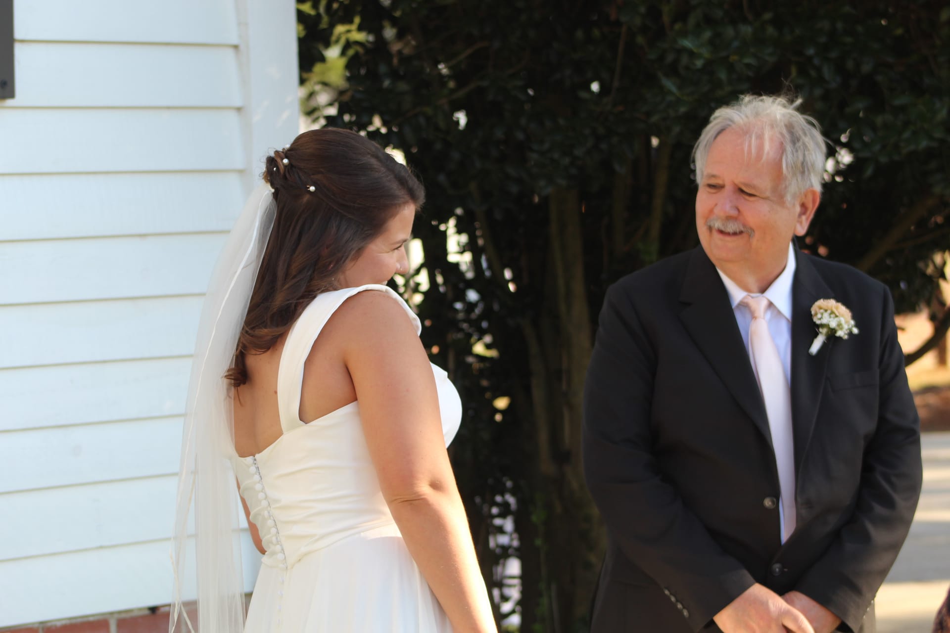 A bride in a white gown and veil shares a tender first-look moment with her father in a dark suit and boutonniere outside the historic white clapboard exterior of Scarborough House.