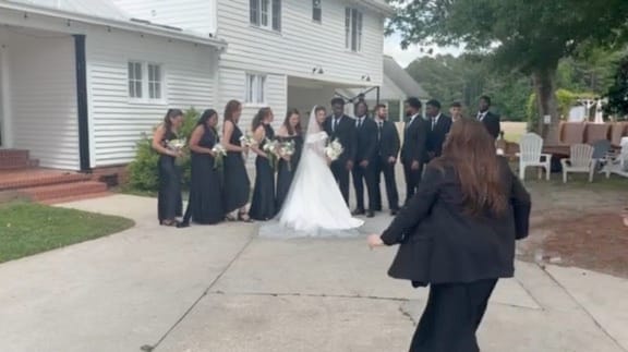 Bridal party dressed in black gowns and suits poses with the bride in a white ball gown in front of the historic 1821 Scarborough House manor on the ceremony lawn.