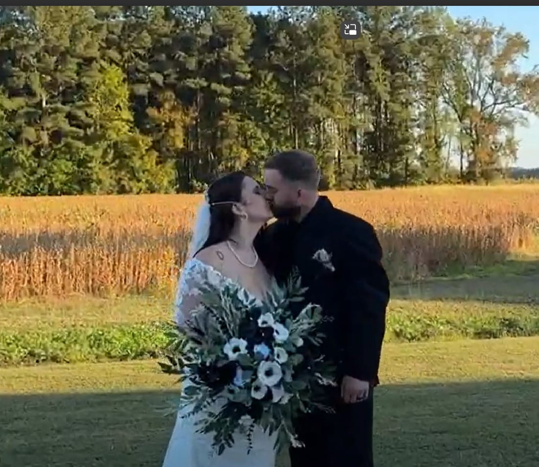 Bride and groom share their first kiss as newlyweds in front of golden autumn farmland fields and tree line at Scarborough House estate venue.