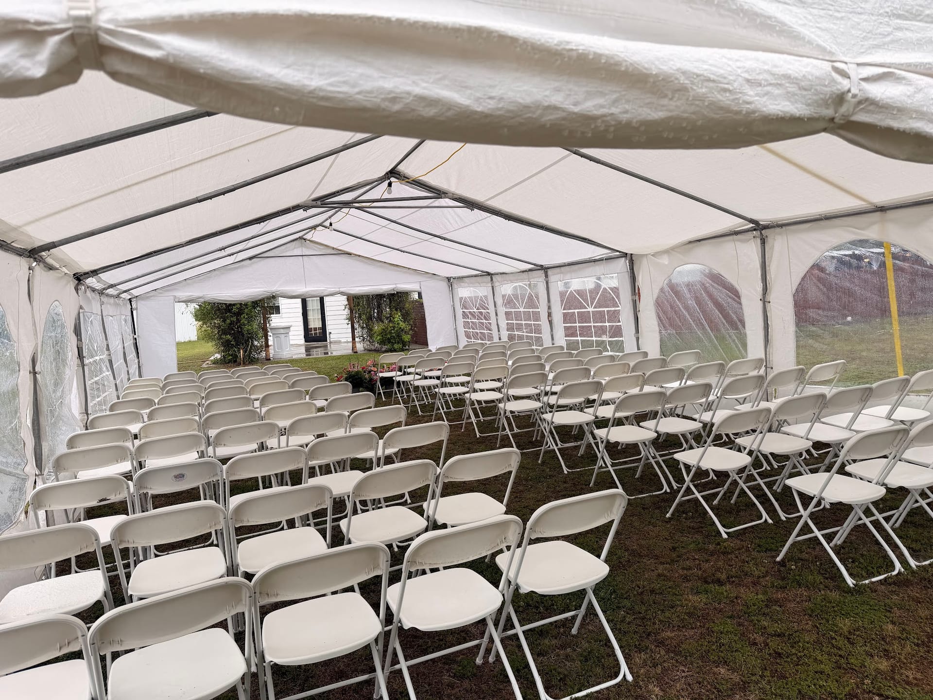 Rows of white folding chairs arranged in a spacious white marquee tent ready for an outdoor wedding ceremony at Scarborough House estate.