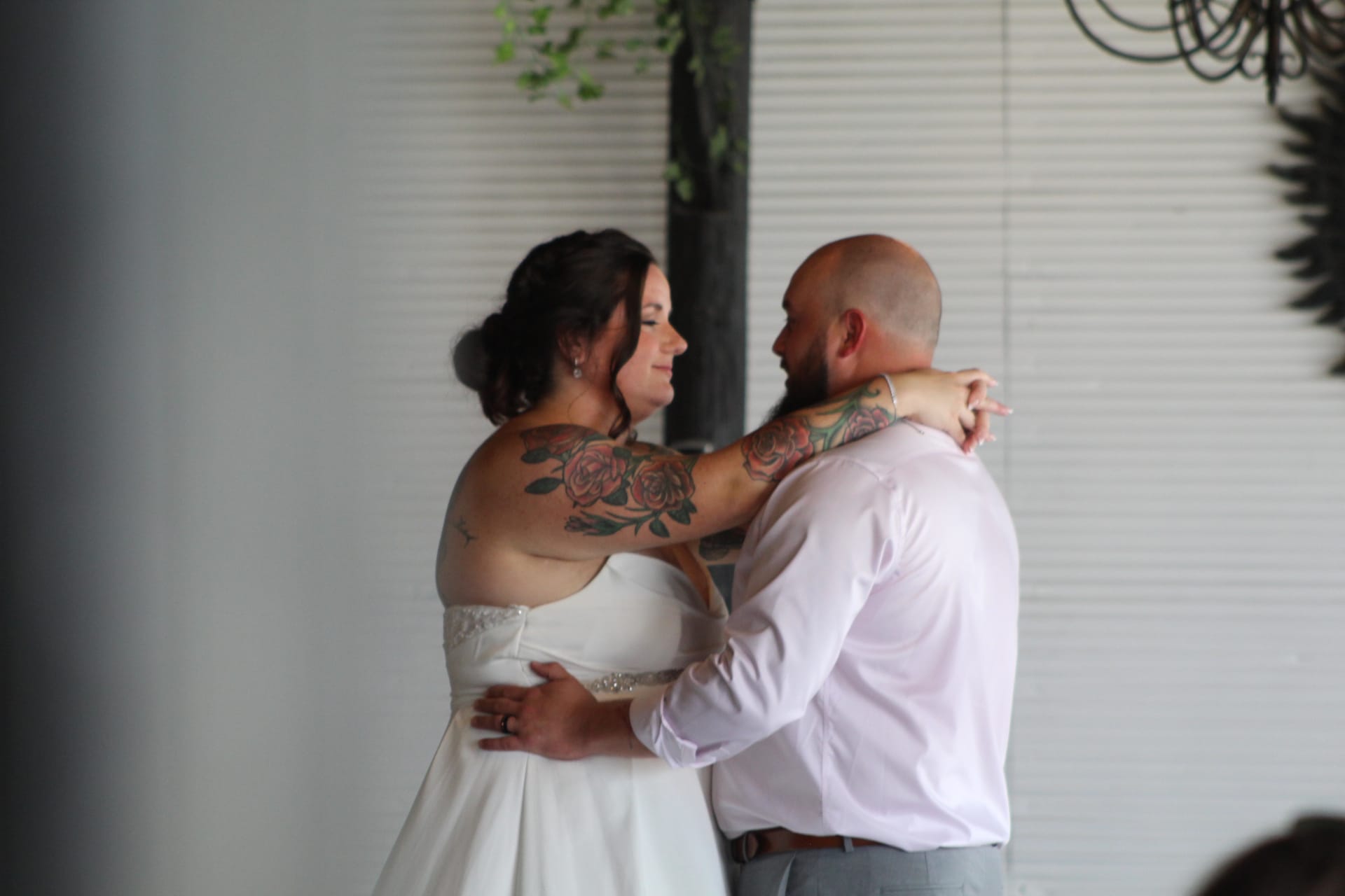 Bride in white gown with floral arm tattoos embraces her groom during their first dance inside the historic grand hall at Scarborough House.