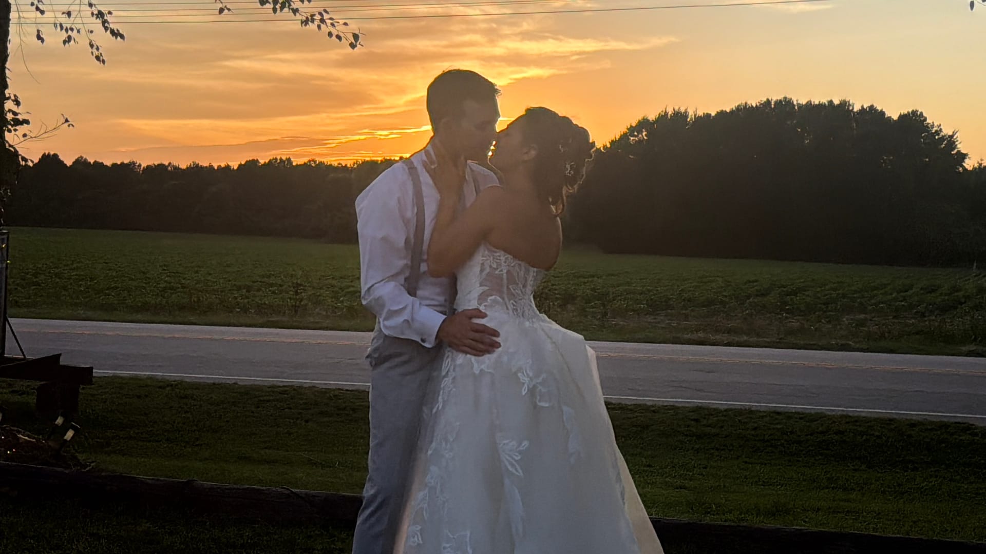 Bride and groom sharing a romantic kiss at golden hour with a glowing orange sunset sky and open farmland fields behind them at Scarborough House estate.