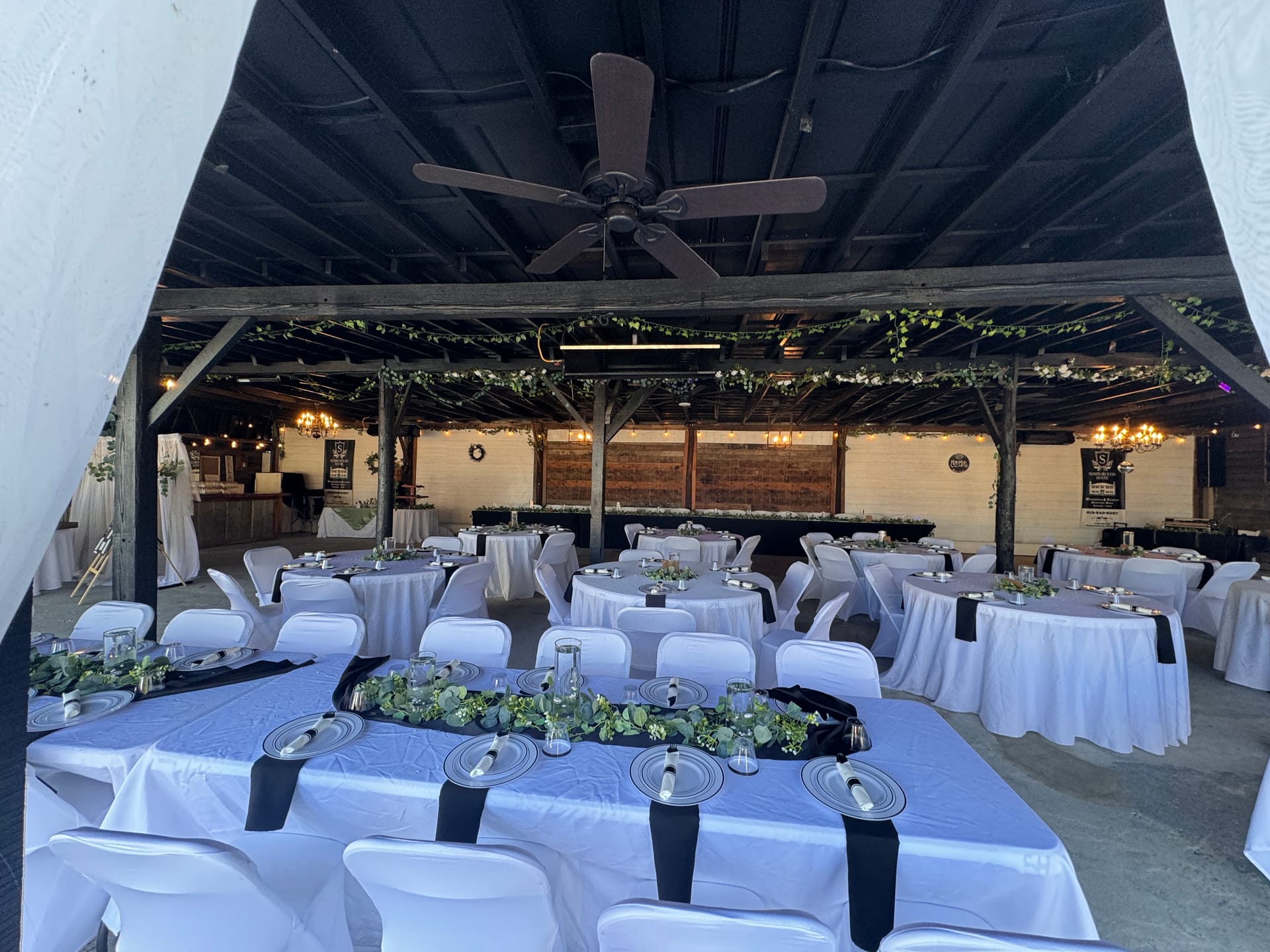 Elegantly decorated grand hall at Scarborough House featuring white linen tables with black napkins, silver charger plates, lush greenery runners, and rustic wooden ceiling beams adorned with trailing vines.