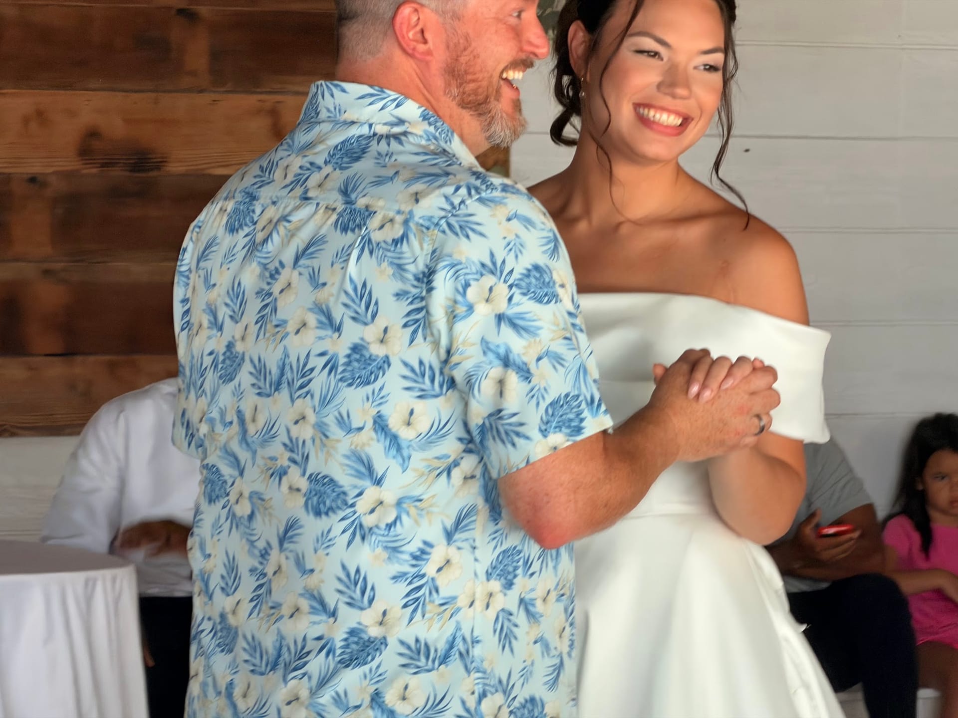 A smiling bride in an off-shoulder white gown shares a joyful first dance with her partner in the grand hall of Scarborough House wedding venue.