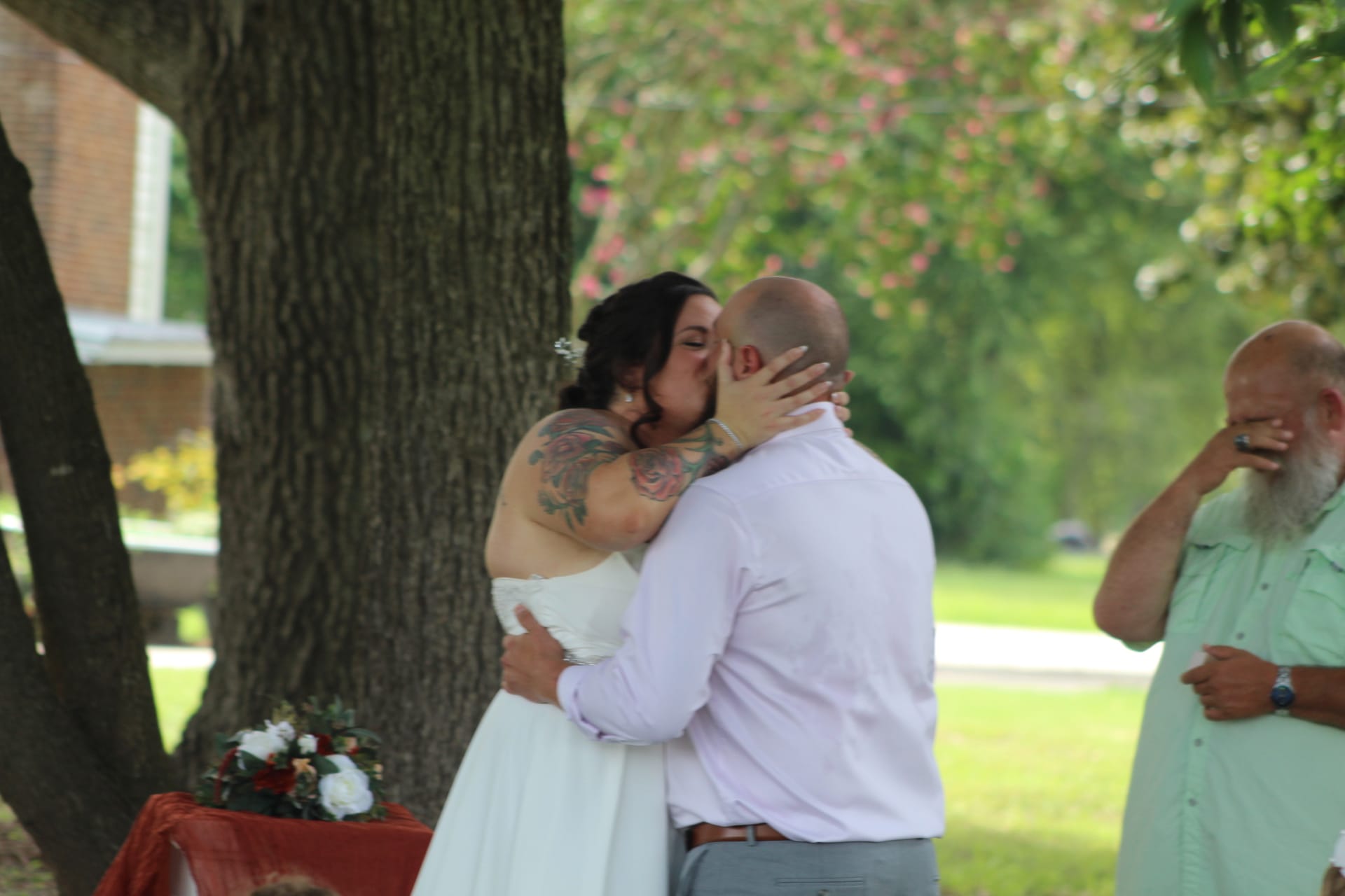 Bride and groom share their first kiss as husband and wife beneath a towering oak tree during an outdoor wedding ceremony at Scarborough House estate.