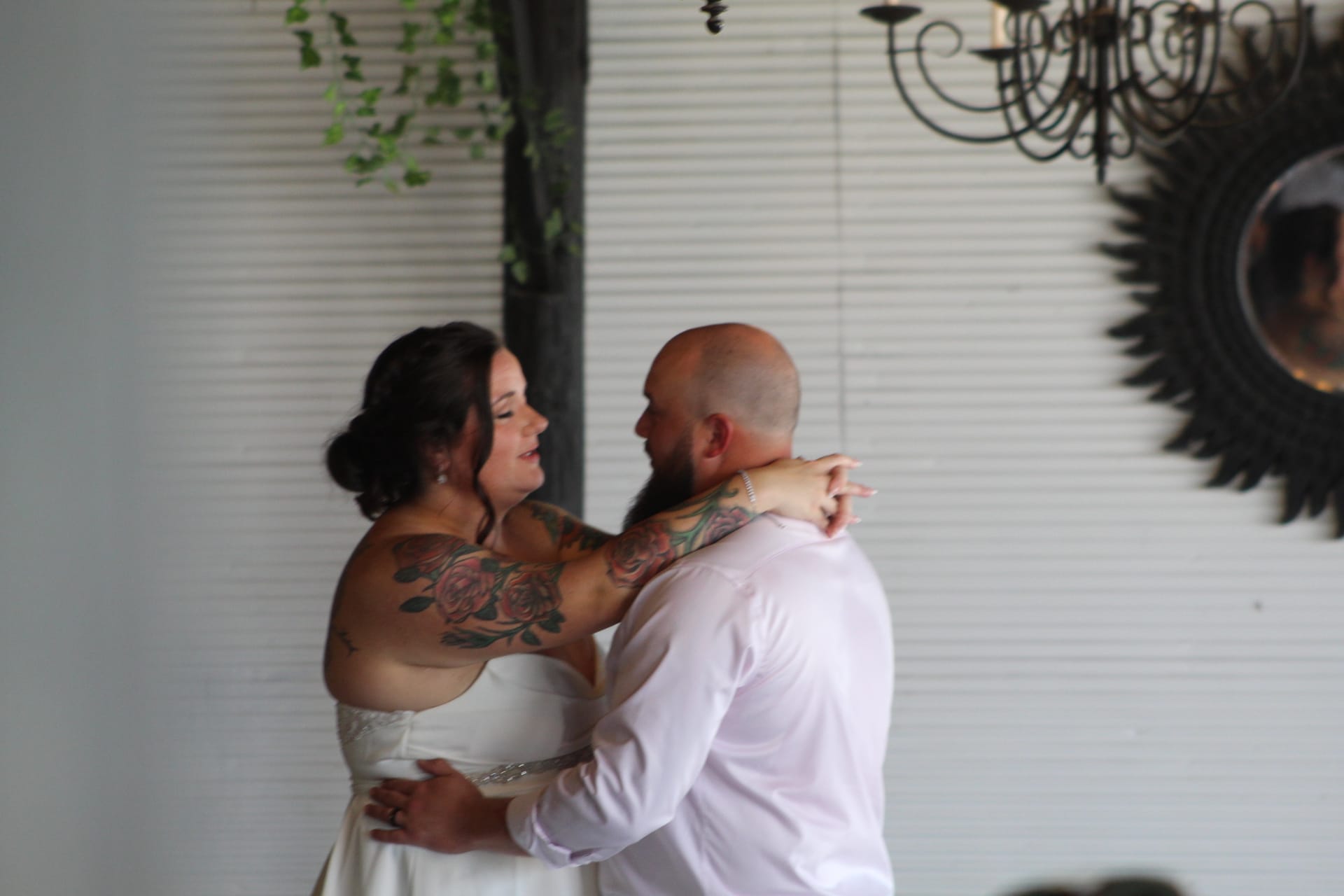 Bride and groom share an intimate first dance inside the grand hall of Scarborough House, with a wrought iron chandelier and white shiplap walls in the background.