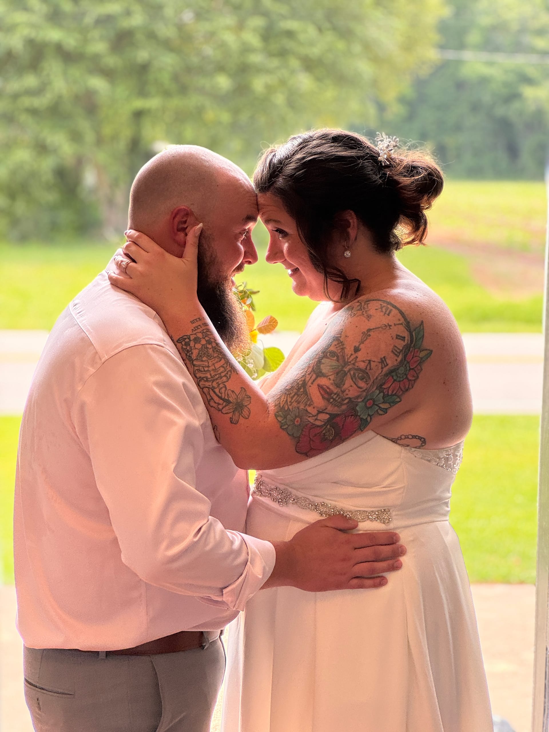 Bride and groom share a tender forehead-to-forehead moment near a sunlit window at Scarborough House, both smiling softly with green grounds visible in the background.