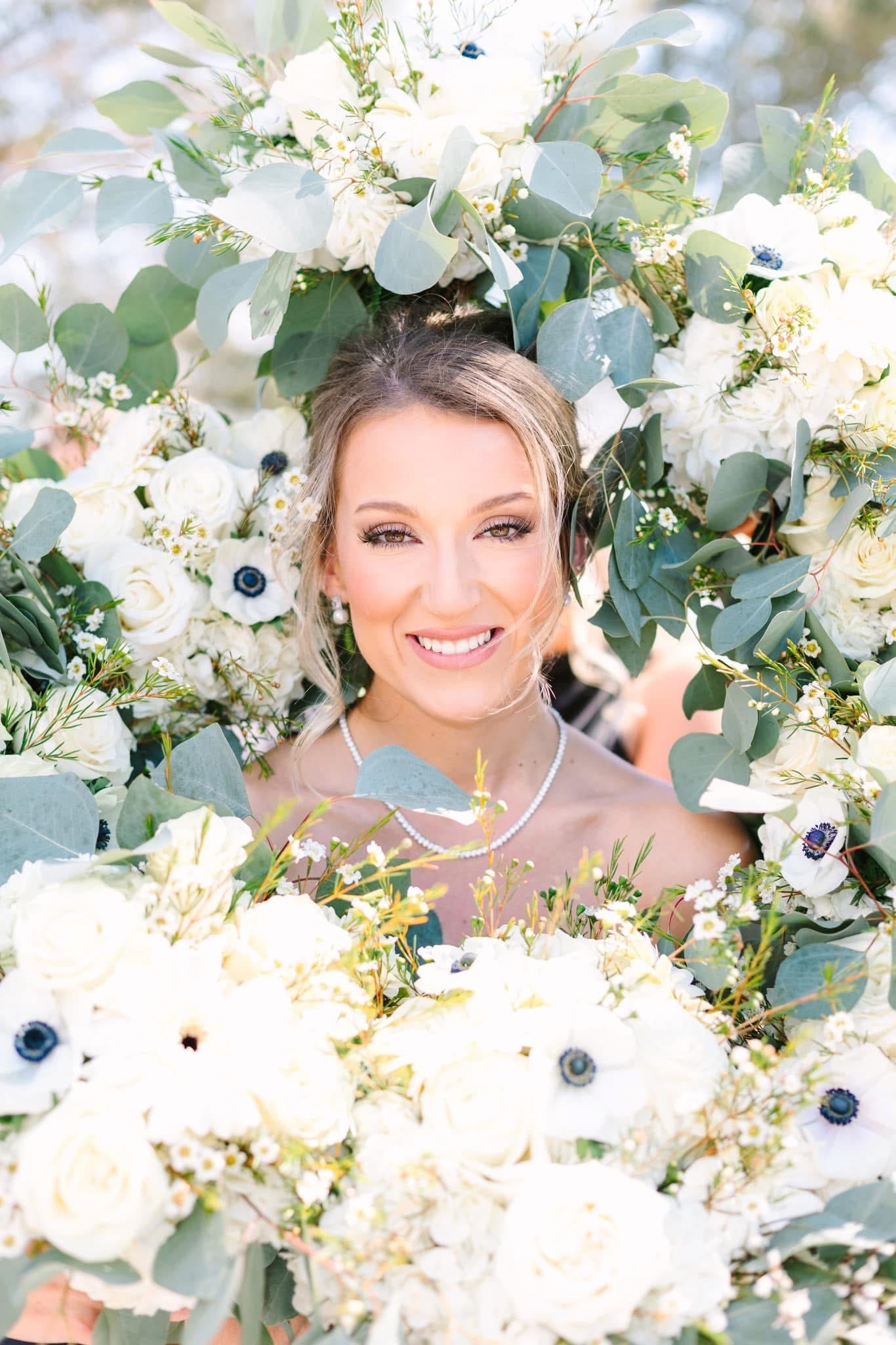 Smiling bride framed by lush white anemone and eucalyptus bouquets in the garden at Scarborough House wedding venue.