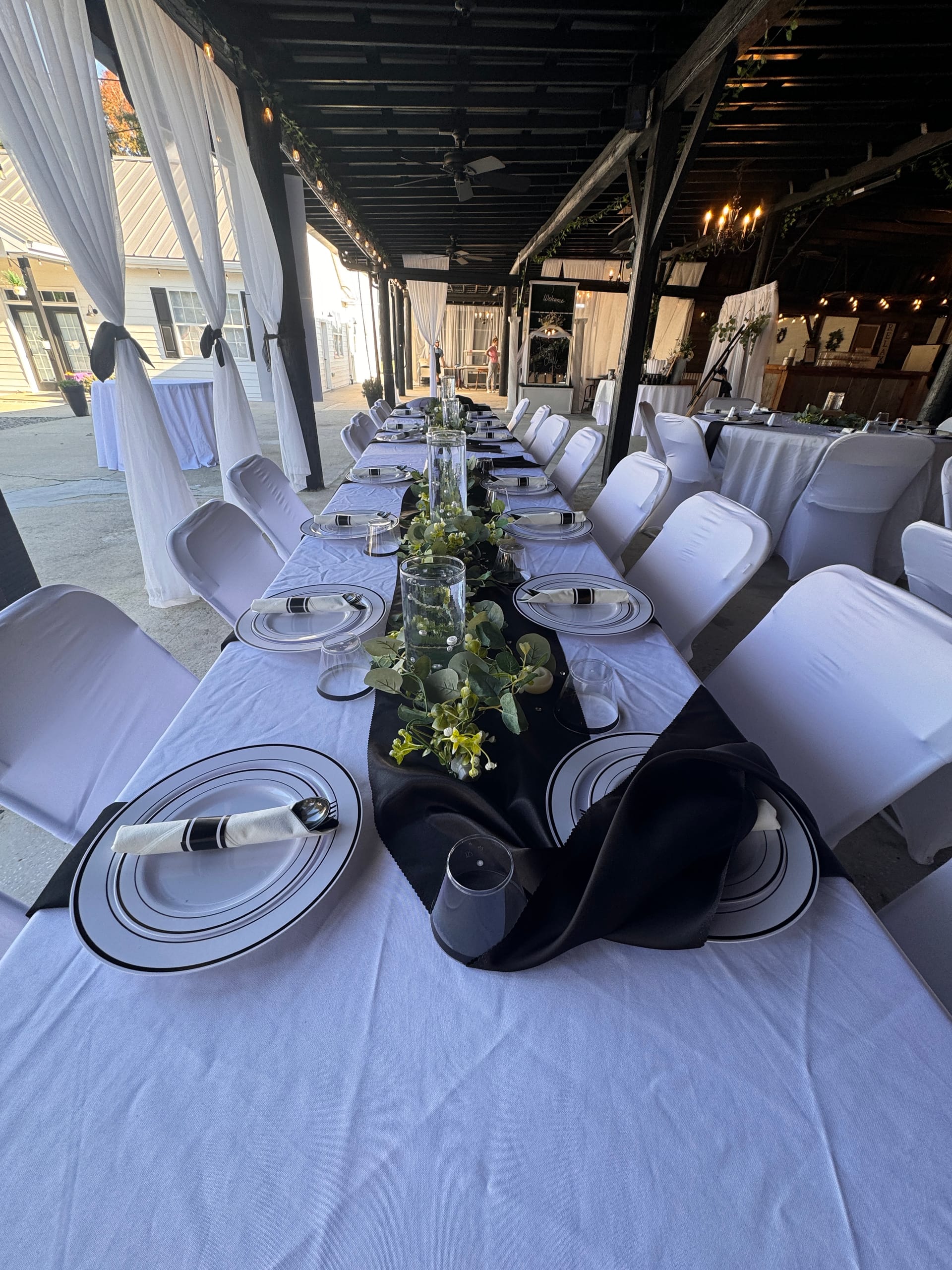 Elegantly set long reception table with white linen, black table runner, greenery centerpieces, and black-trimmed plates under the covered magnolia pavilion at Scarborough House.