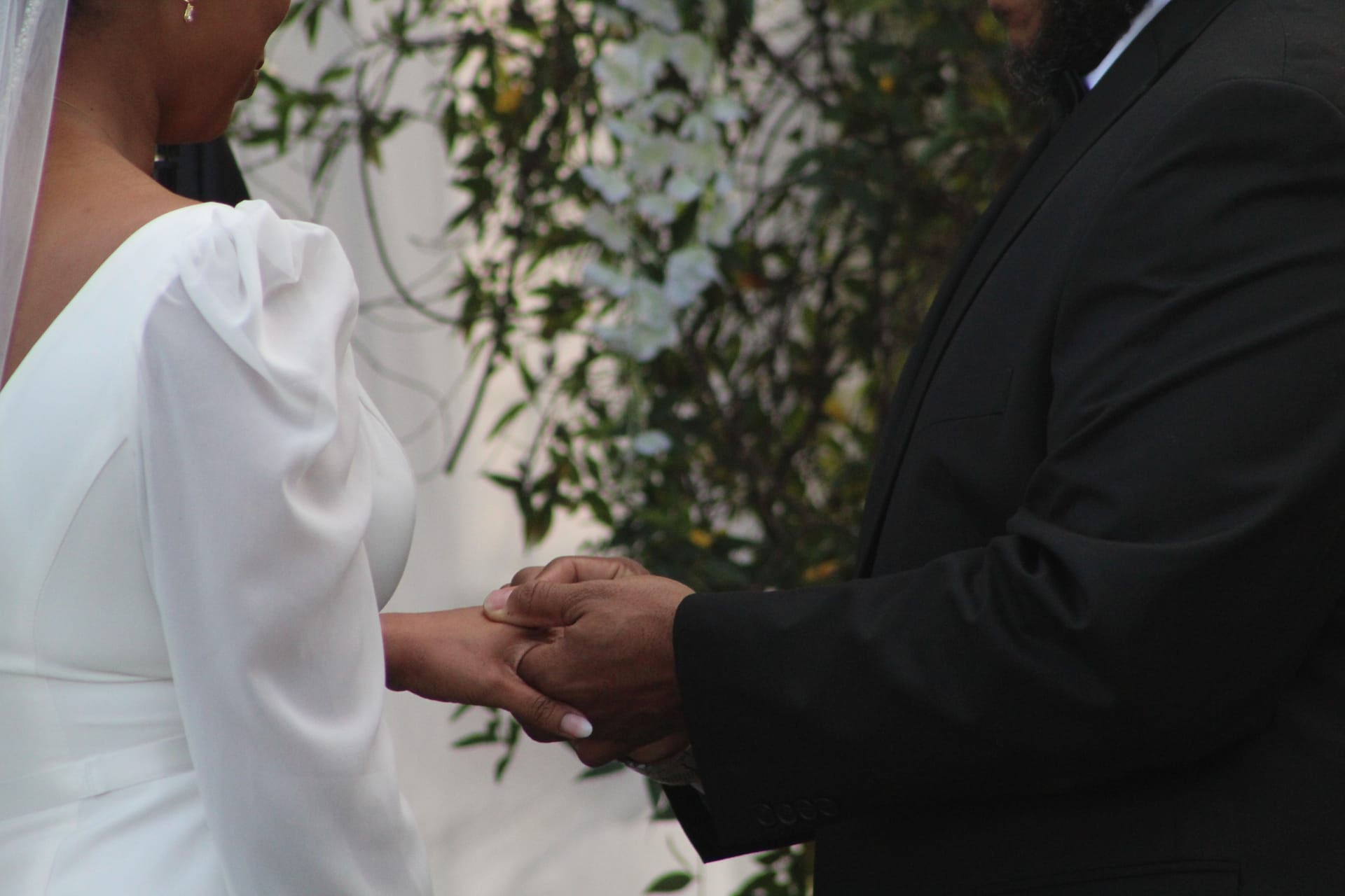 Groom placing a wedding ring on the brides hand during an outdoor ceremony at Scarborough House with a lush green and white floral backdrop.